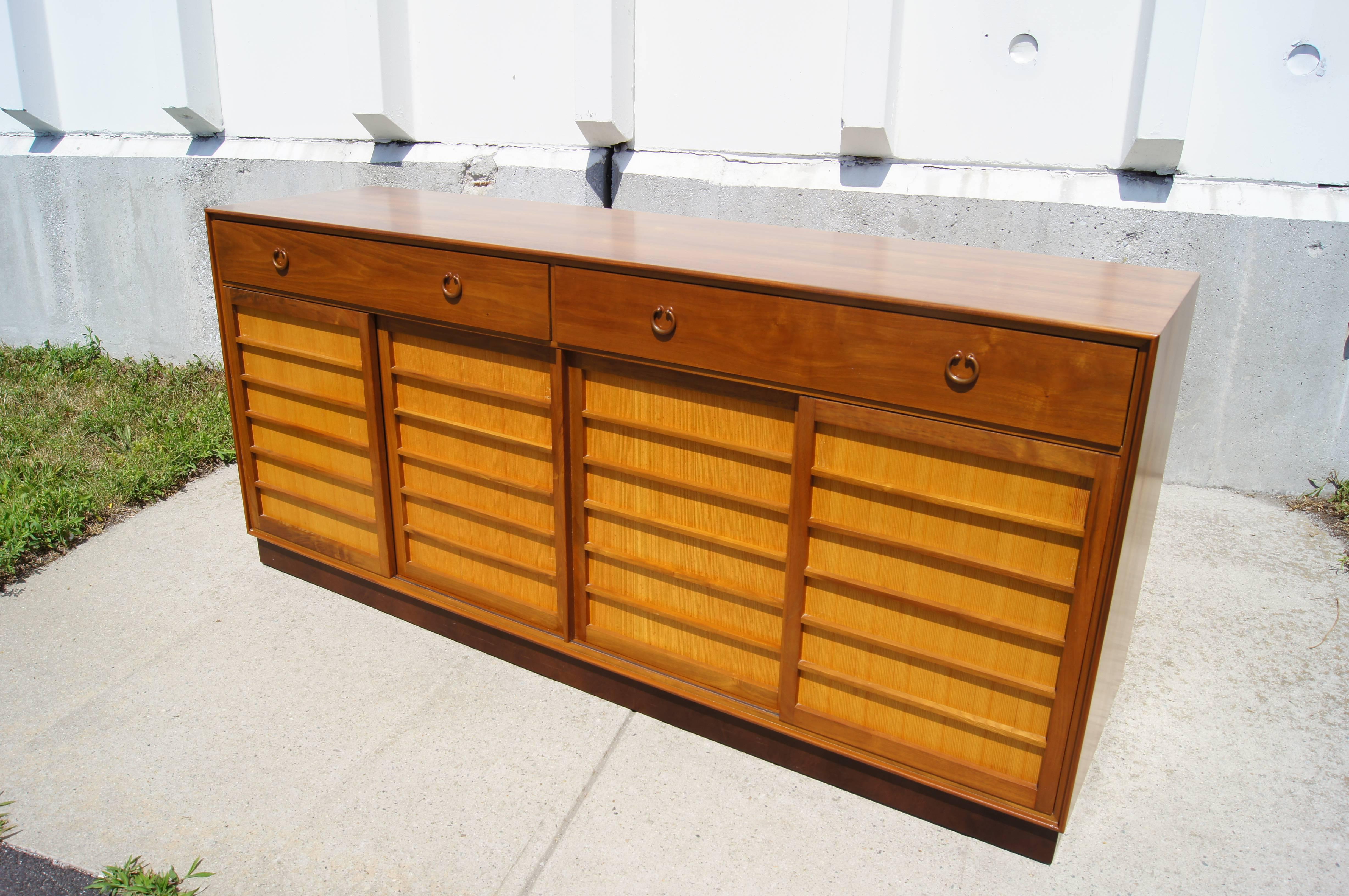 Edward Wormley designed this handsome sideboard, model 671A, for Dunbar in 1953. The case features Japanese fir panels that contrast with the walnut frame.  Two top drawers, one of which is divided, open with round bronze pulls. Behind the four