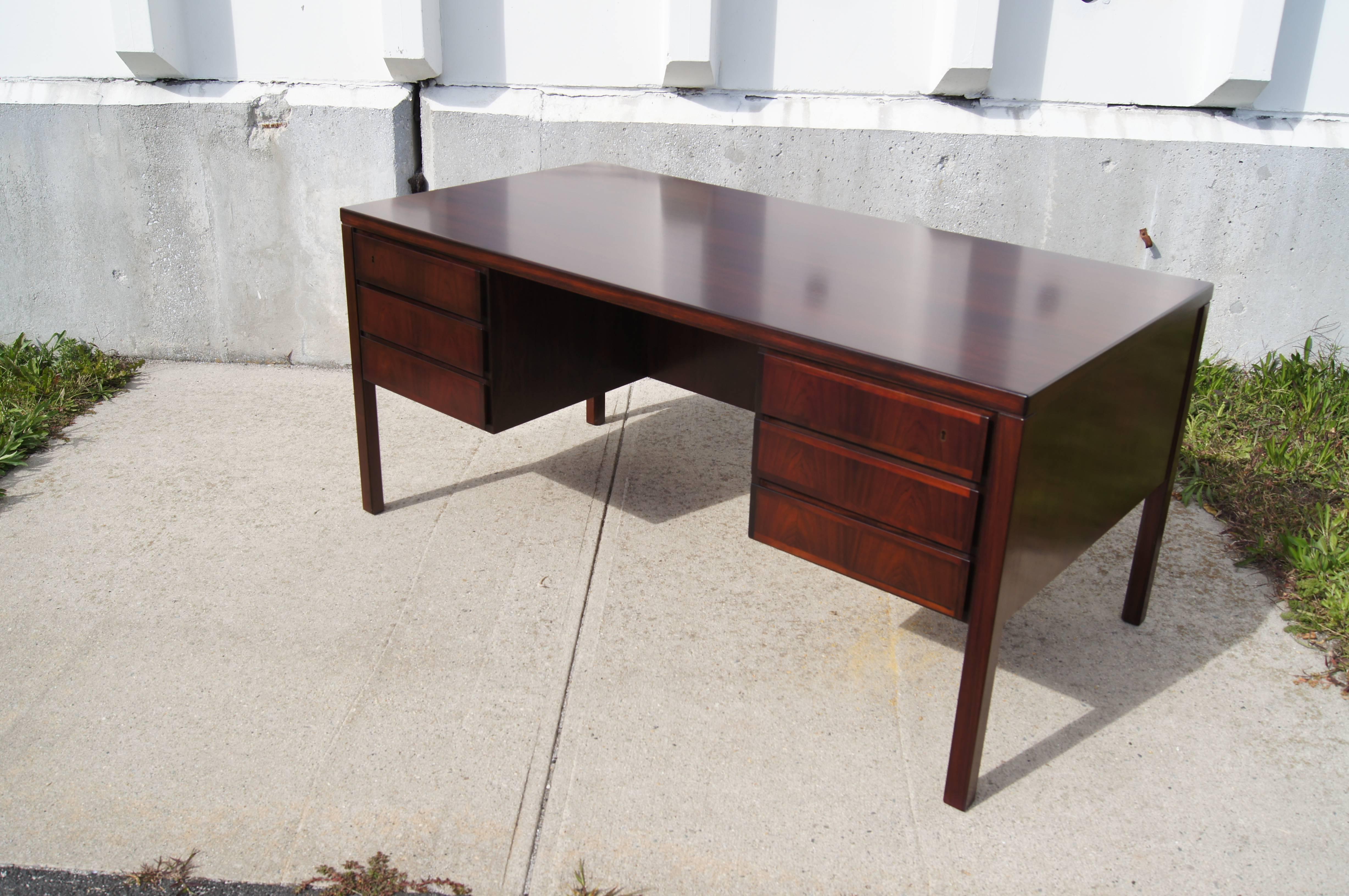 Handsome from every angle, this double-sided rosewood desk by Gunni Omann for Danish cabinetmaker Edmund Jorgensen positions three drawers to either side of the chair opening. On the finished back, two ample storage spaces bracket a drop-down door