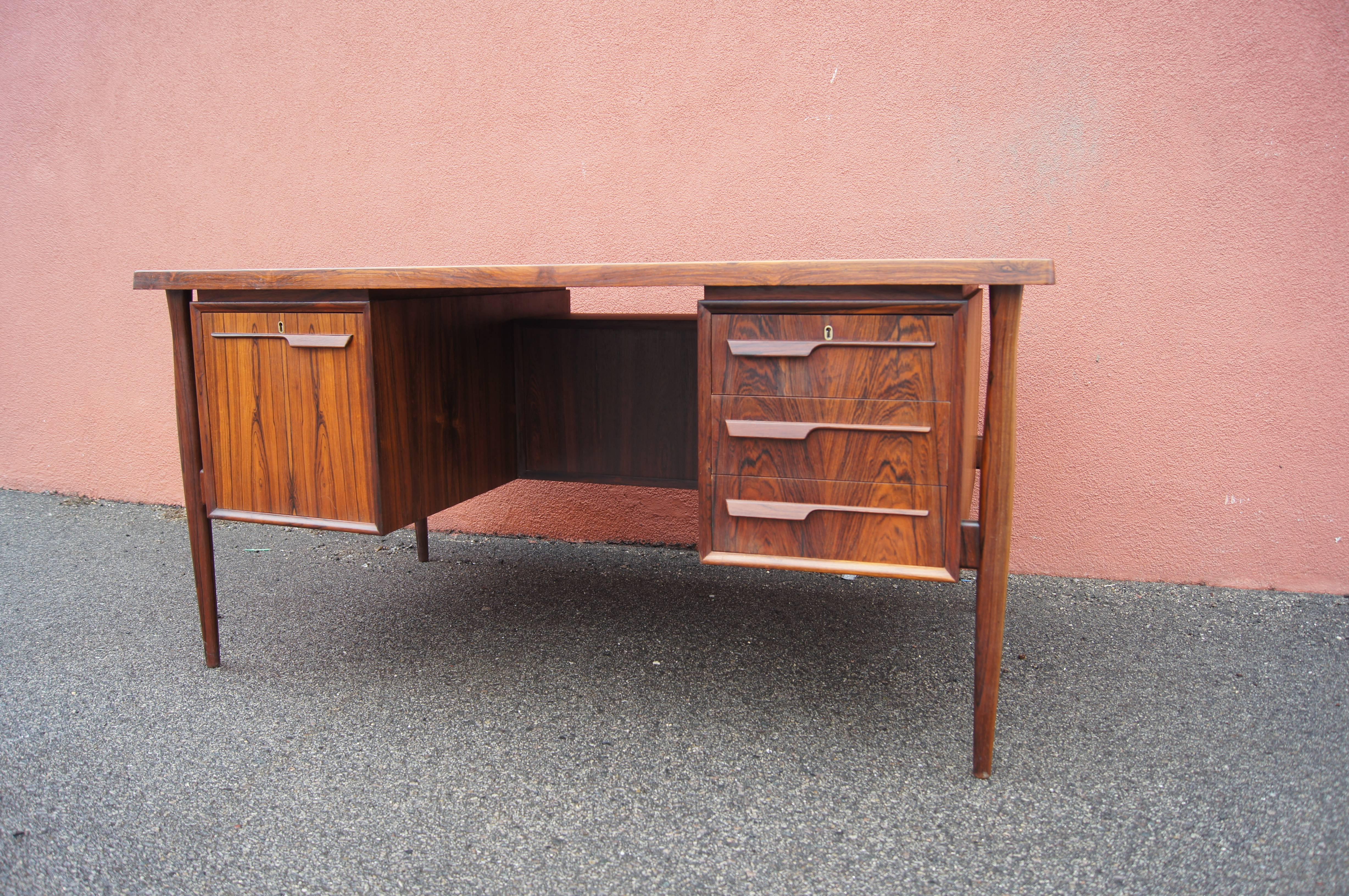 This handsome rosewood desk was designed in the 1960s by Danish master Arne Vodder. Flanking the chair opening are a file cabinet and three drawers. The front offers more storage, concealed on either side of the central shelves behind hinged