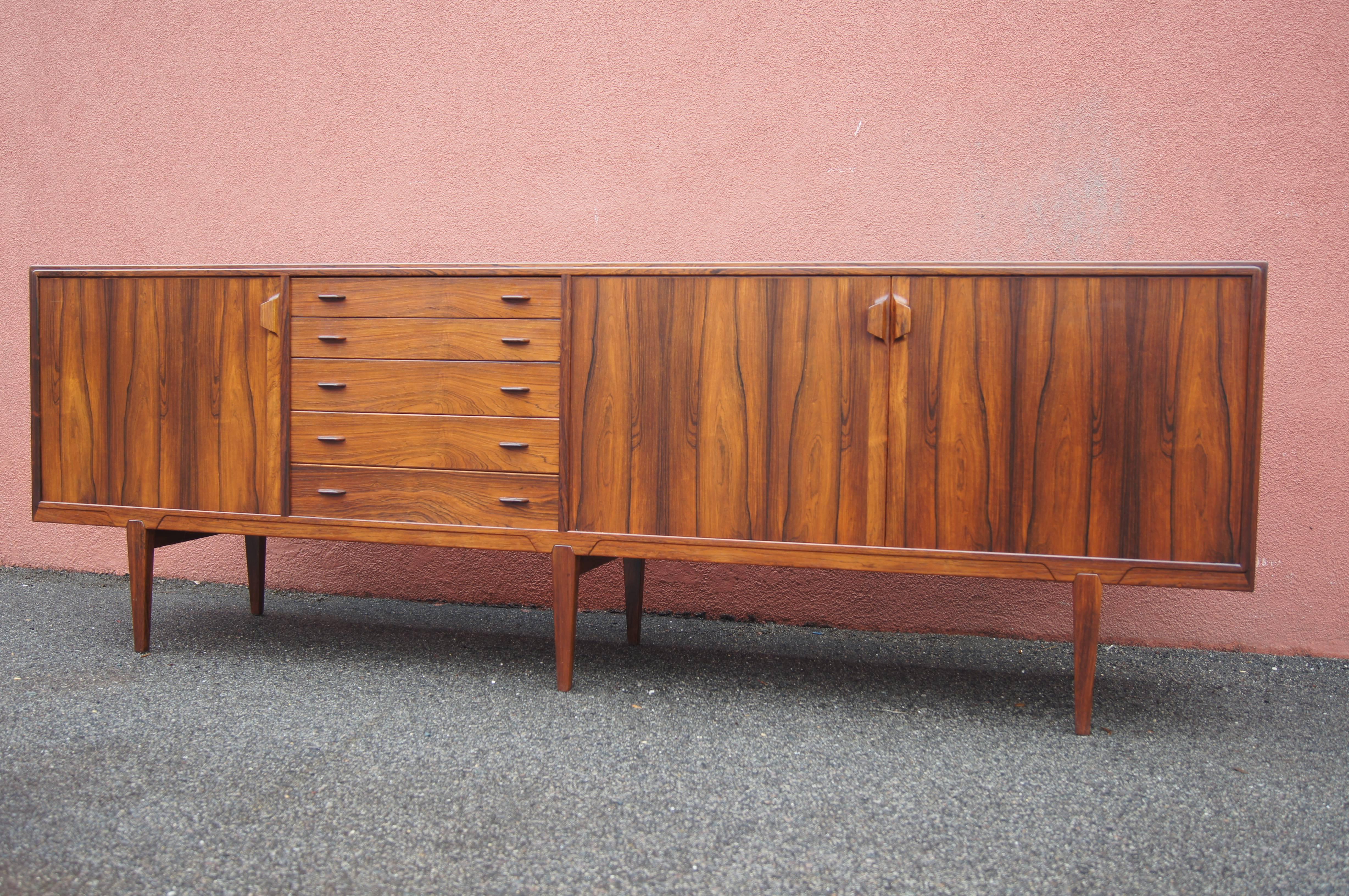 Designed by Henry Rosengren Hansen for Brande Møbelindustri, this gorgeous six-legged sideboard features an eye-catching rosewood grain. It offers plentiful storage, with five drawers and movable shelving behind three doors with carved handles.