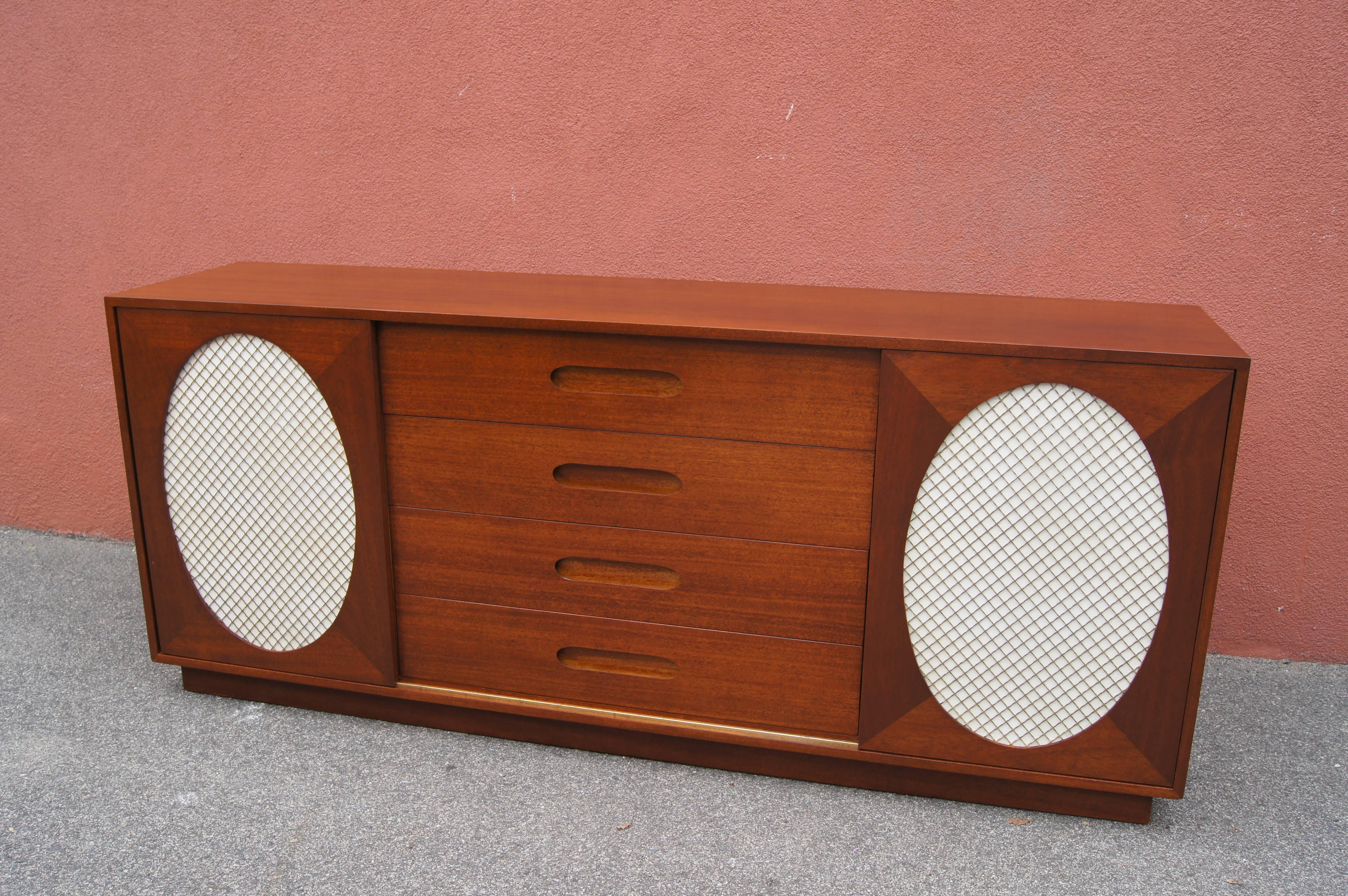 This is a striking version of one of Harvey Probber's 1950s mahogany sideboards. At center are four large drawers with wide inset handles; the top drawer is divided into five sections and the one below into three. Two sliding panels with oval mesh