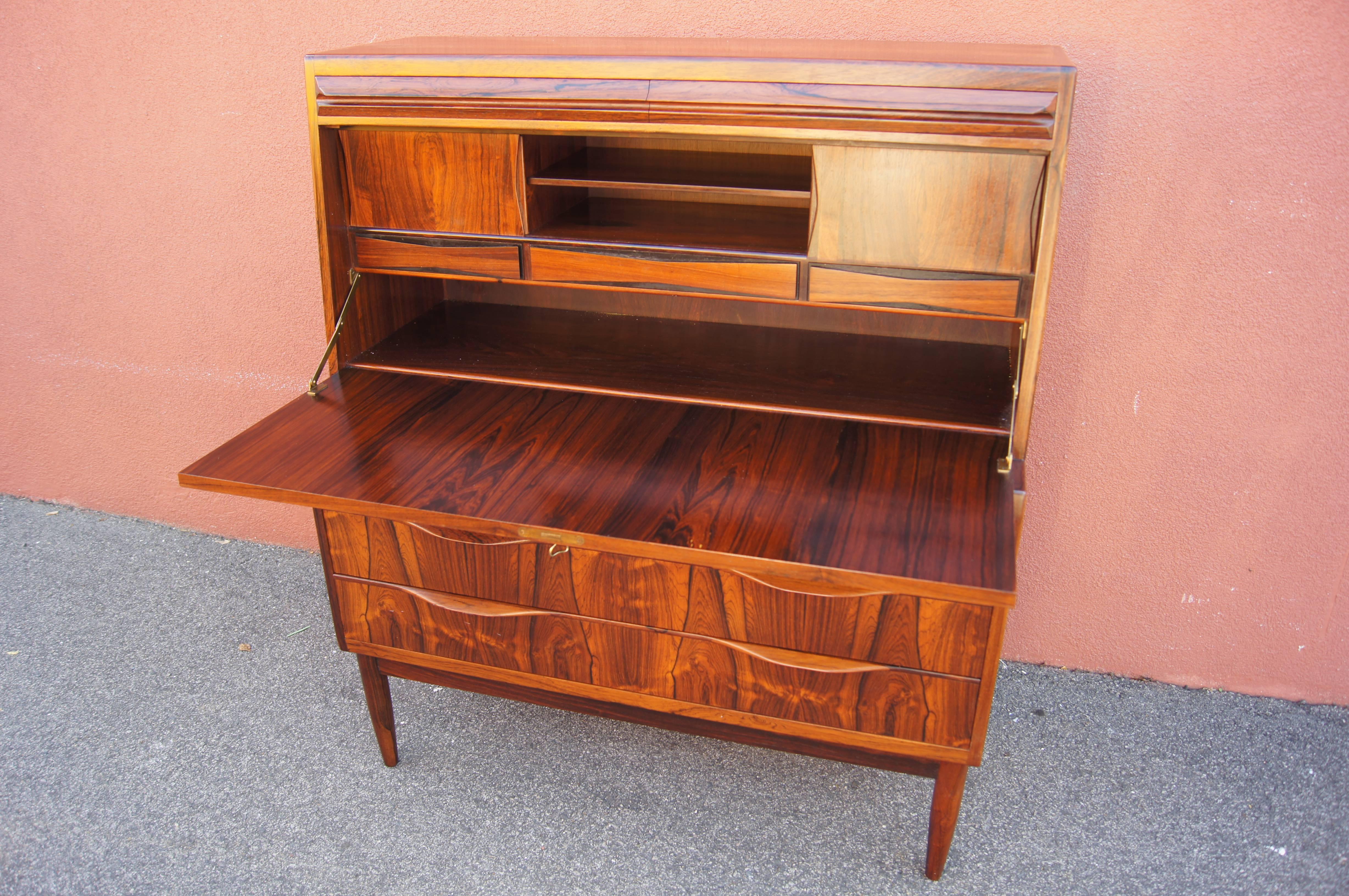Designed by Ib Kofod-Larsen, this Danish modern secretary desk has been crafted from rosewood with beautifully matched grains. The locking desktop folds down, revealing a wide shelf, three drawers with bowtie fronts, and three small cubby spaces