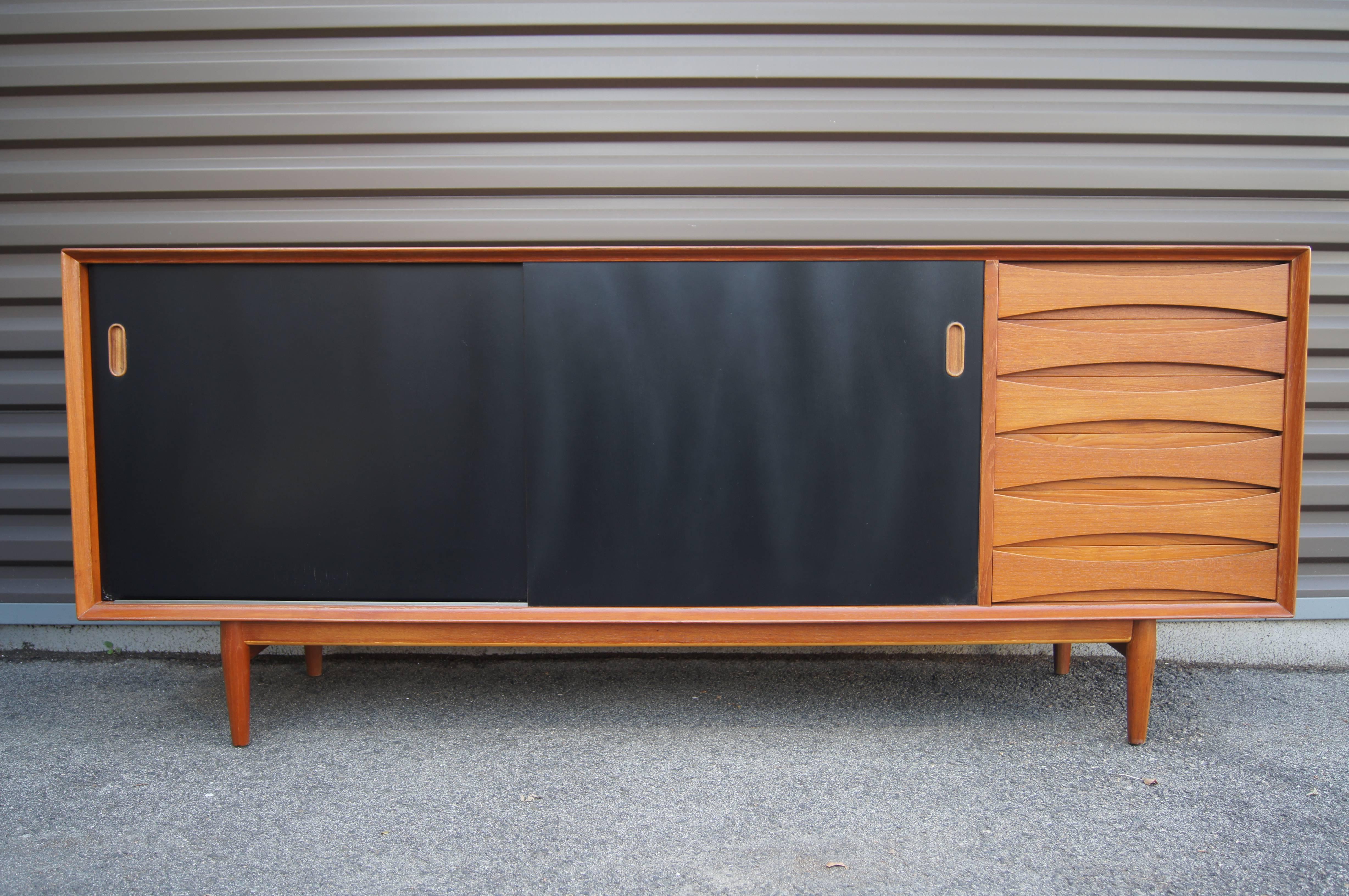 Designed by Arne Vodder for the Danish furniture company Sibast, this modern sideboard comprises a teak case on a plinth base. The sliding doors are reversible to any combination of teak or black lacquer fronts; inside the shelves are adjustable. To