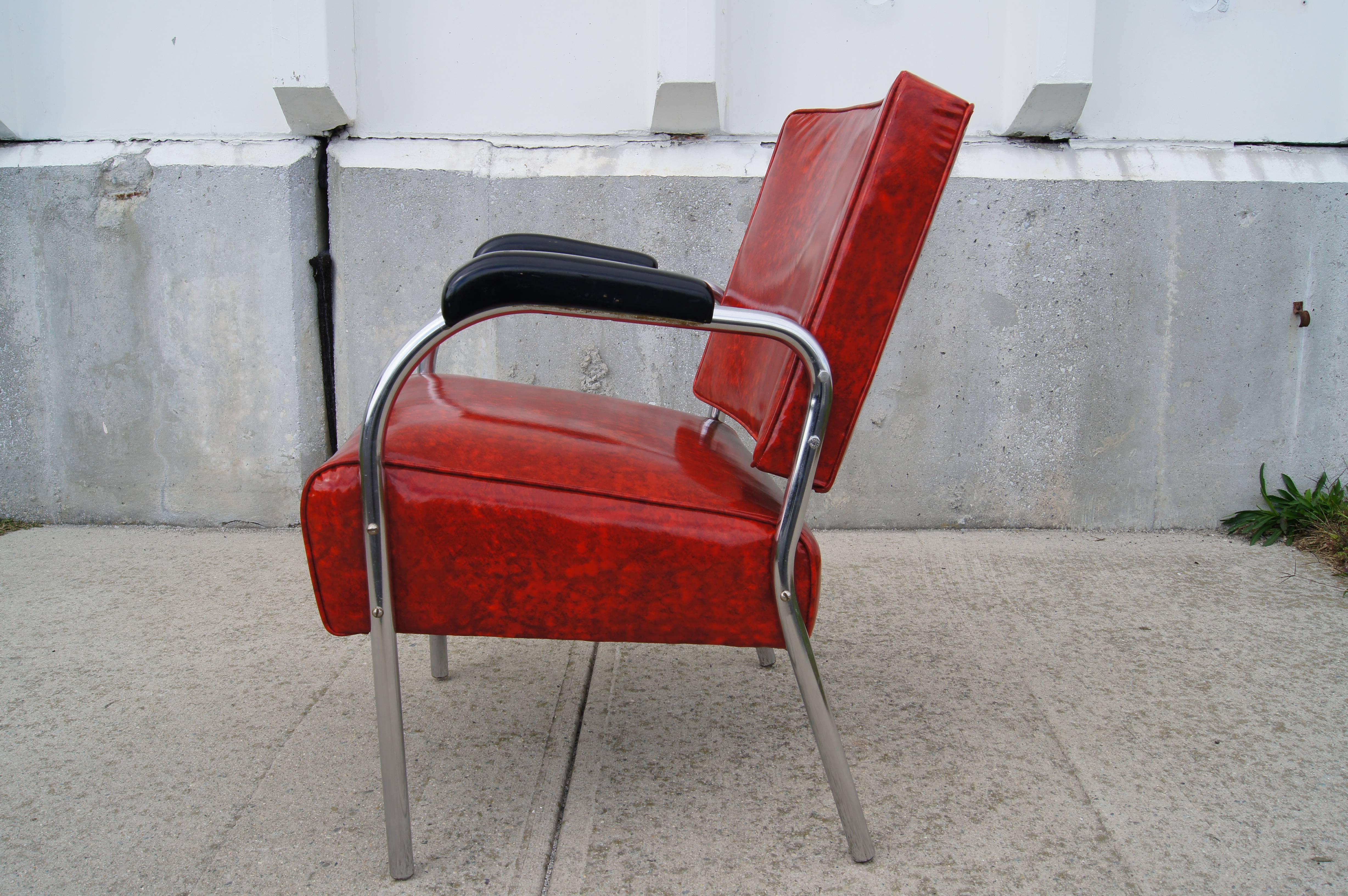 This 1940s moderne armchair was produced in the United States. The tubular chrome frame features black resin armrests; the comfortable seat and backrest has been newly reupholstered in vintage Naugahyde in a brilliant ruby red.

We have five