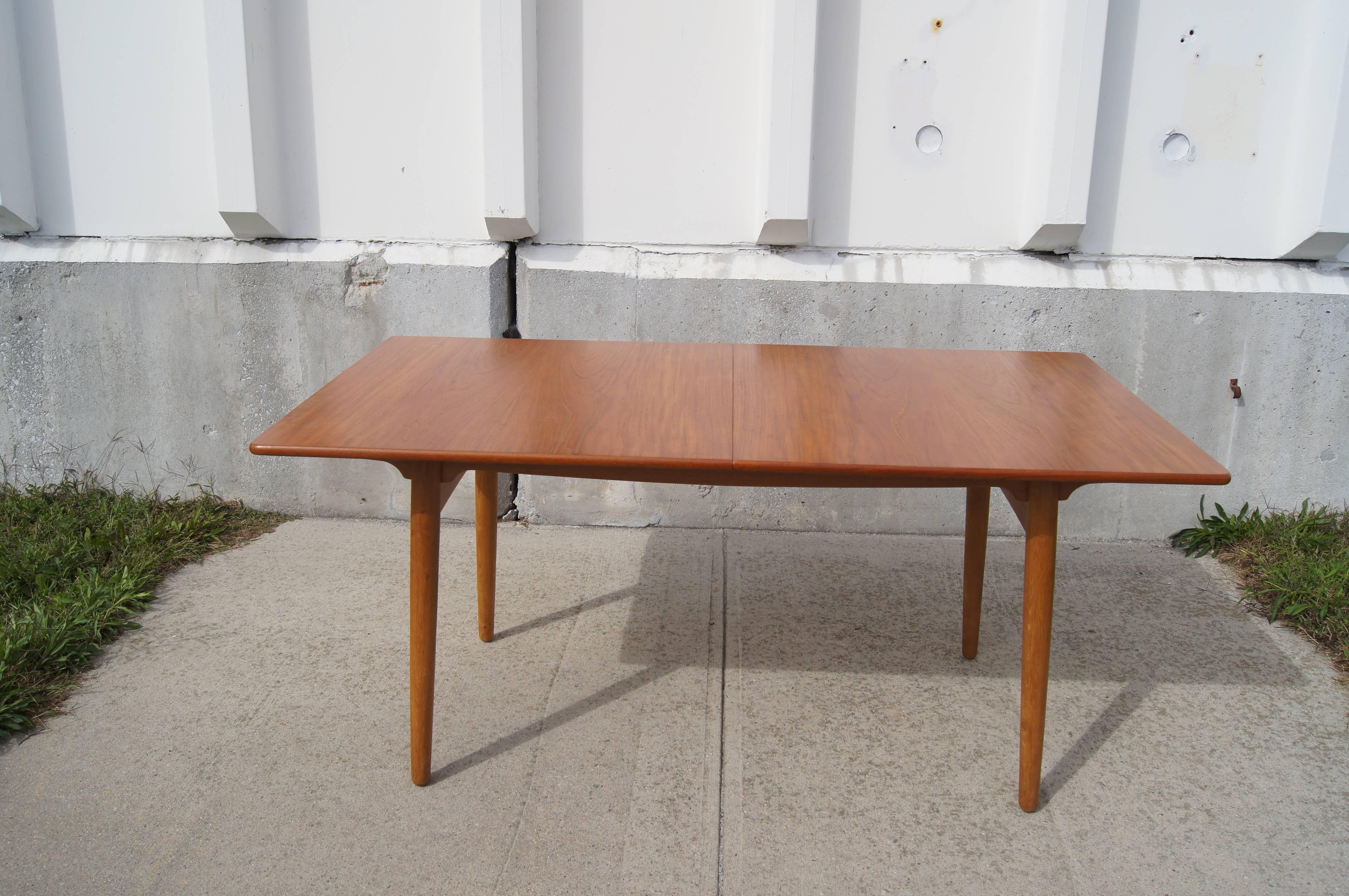 Hans Wegner designed this dining table, model AT310, for Danish manufacturer Andreas Tuck. It comprises a teak top with oak legs and base. The table includes two 15.75