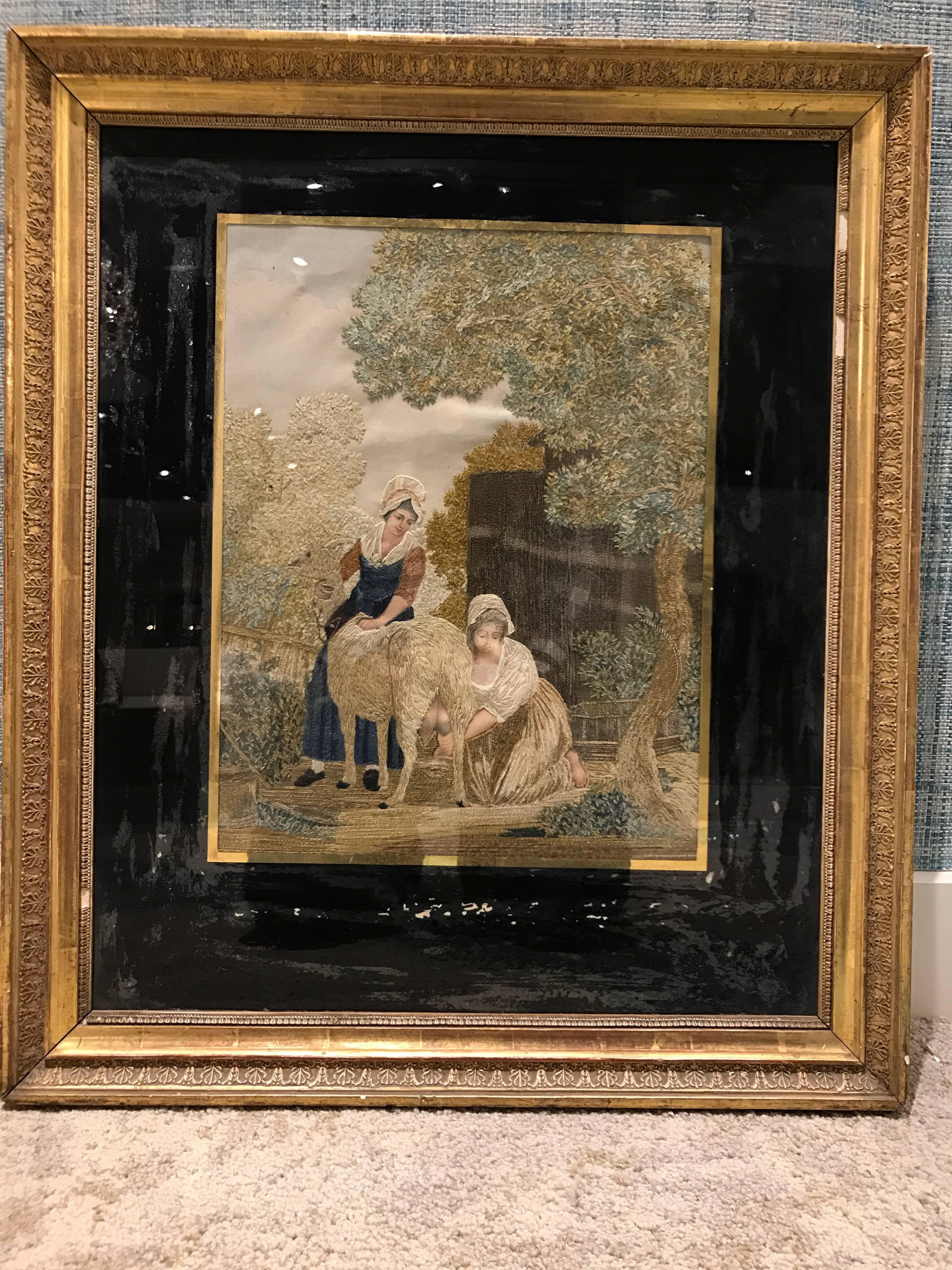 An unusual framed silk needlepoint of two women with goat. Reverse painted glass in giltwood frame.