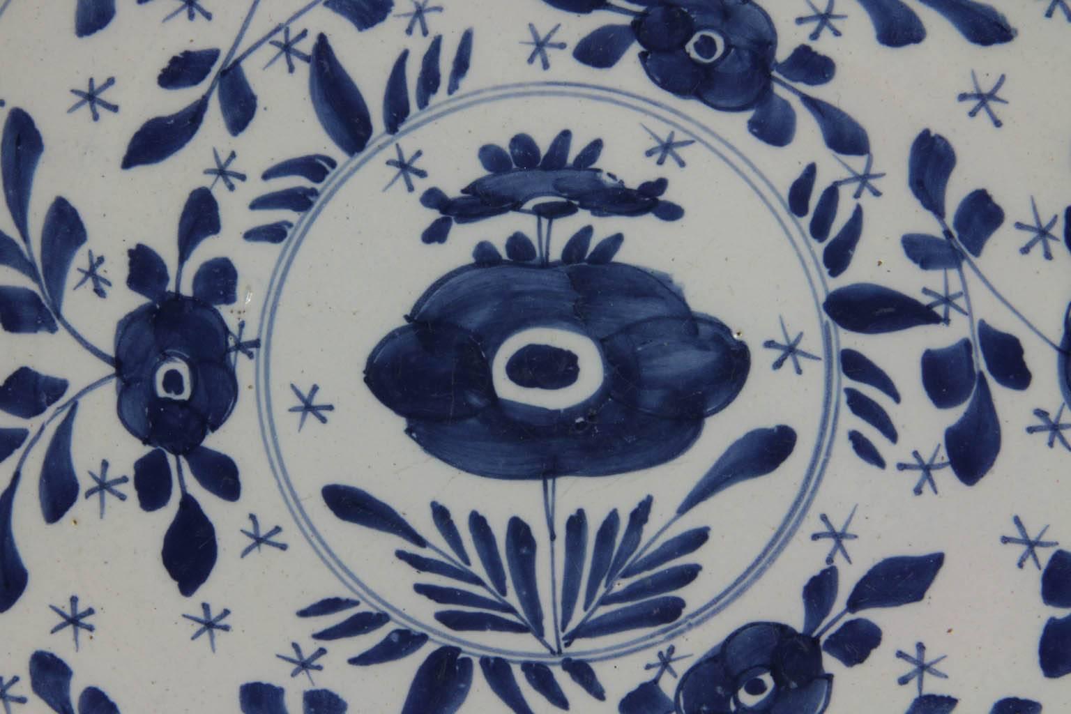 Large delft blue and white plate with central flower and surrounded by small flowers and leaves.