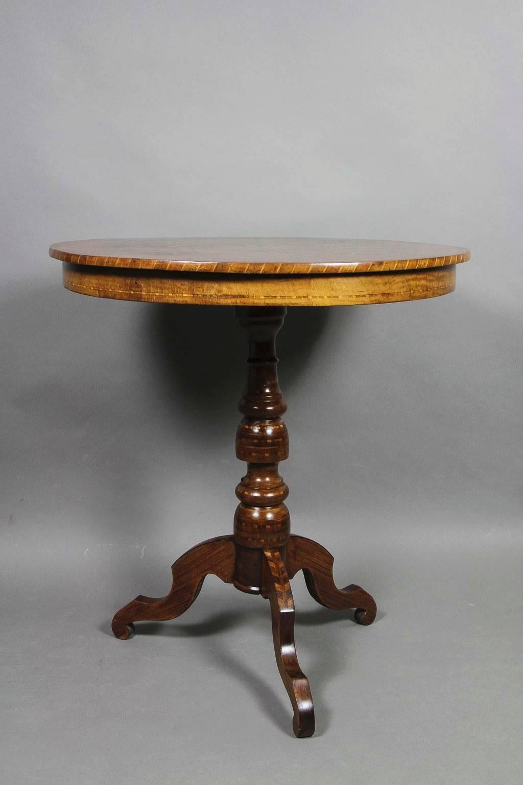 Circular top with radiating starburst inlay on a turned support ending on tripartite legs.