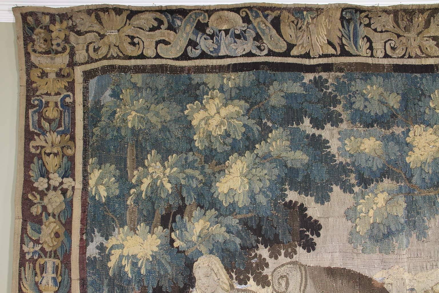 Rechteckig mit Blatt-, Blumen- und Vasenbordüre, die Szene zeigt einen Mann, der Brot im Ofen backt, eine Frau, die an einem Tisch steht, und Kinder, die mit einer Burg im Hintergrund und Bäumen und Pflanzen im Vordergrund herumtollen.