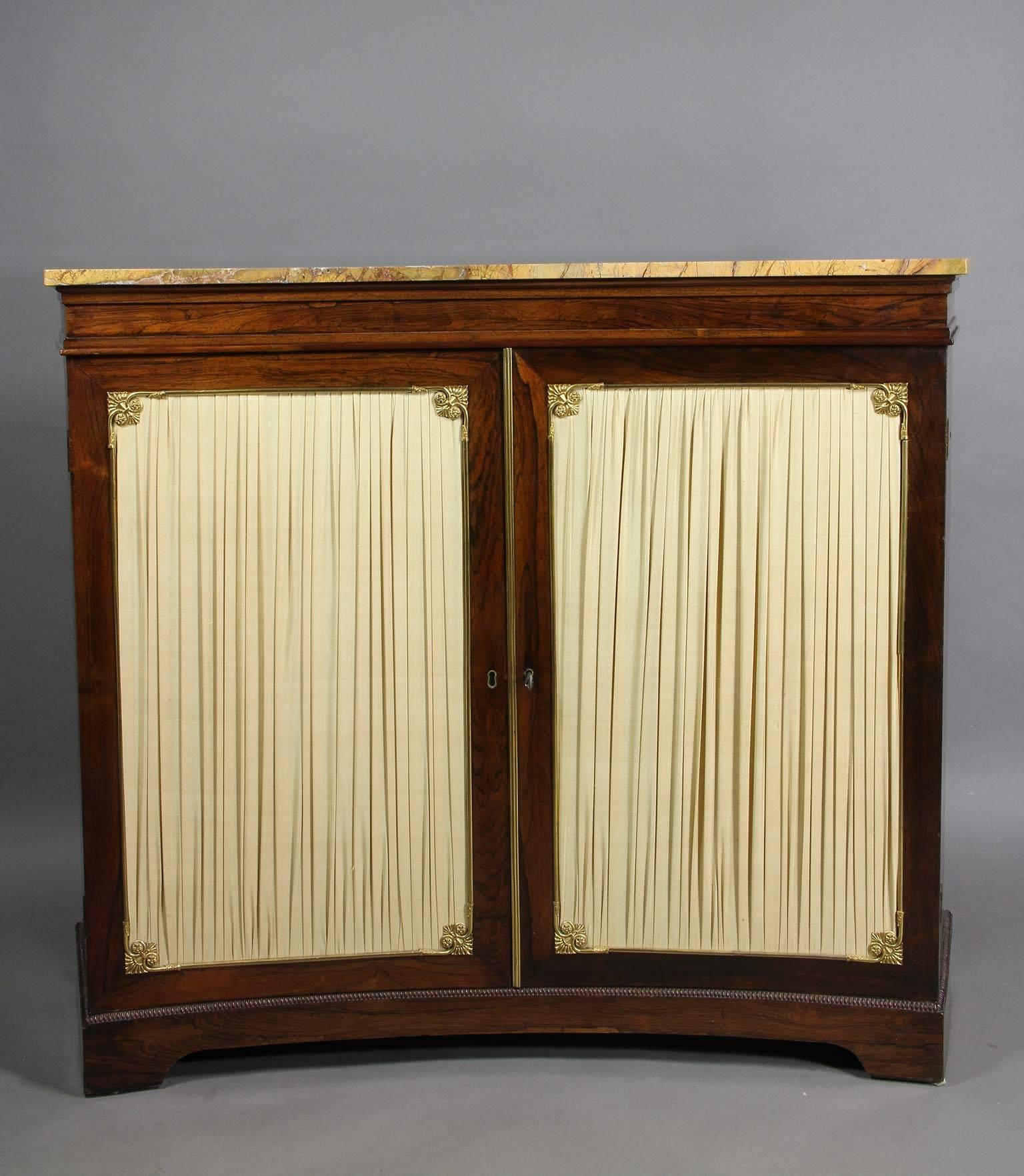 Of concave form with yellow marble top over a pair of pleated doors enclosing a shelf, bracket feet.