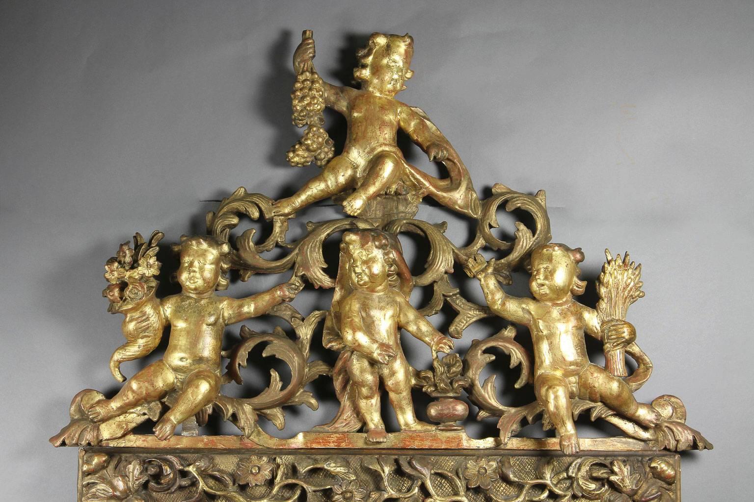 The arched top carved with four figures representing the Four Seasons with their attributes within an acanthus scroll background , the old beveled mirror plate set in a carved cushion form frame carved and decorated with flowers and trailing vine.