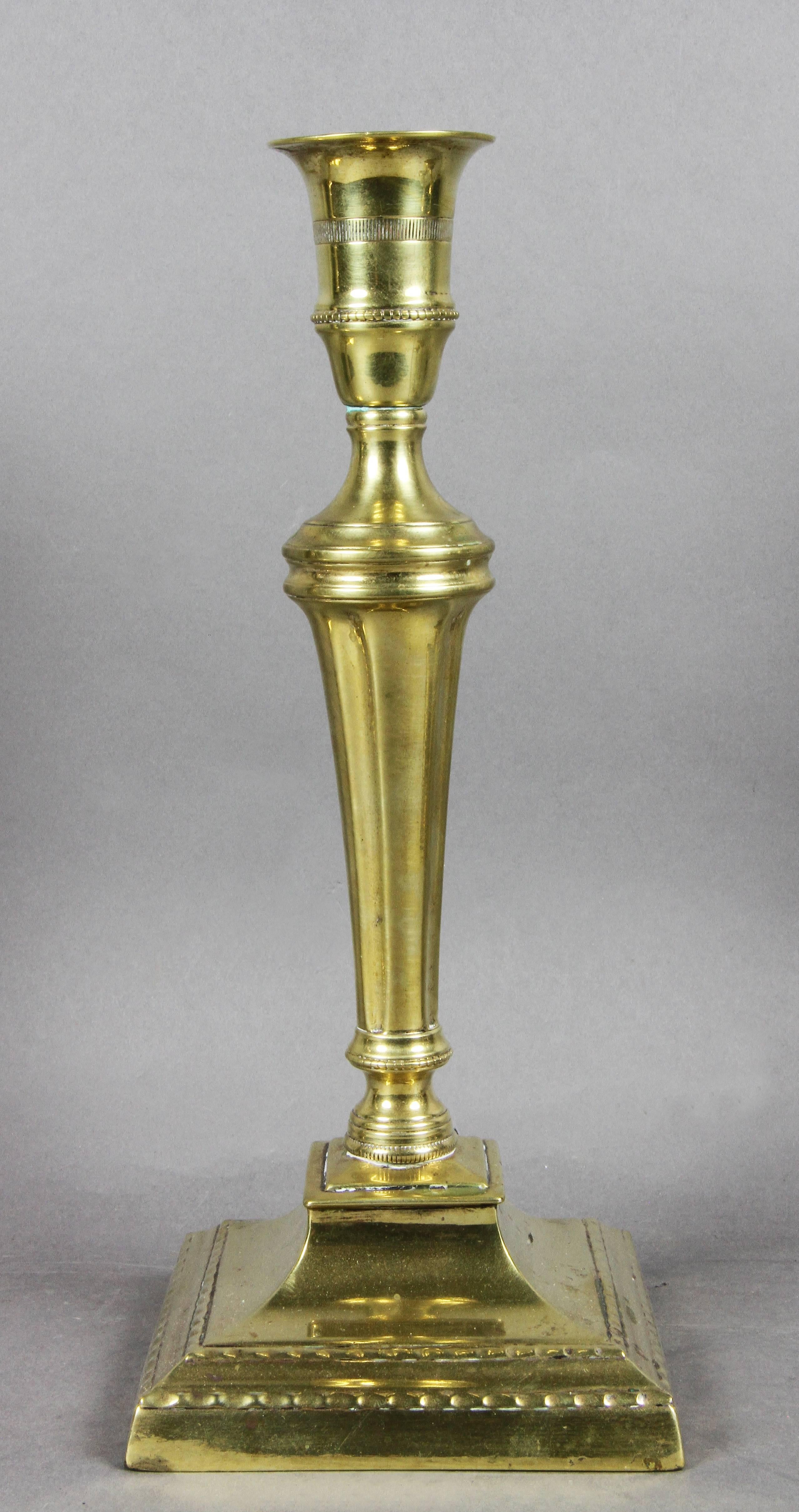 Each with flared candleholder with beaded decoration and engine turning, tapered fluted support joining a stepped square base with gadrooned edge.