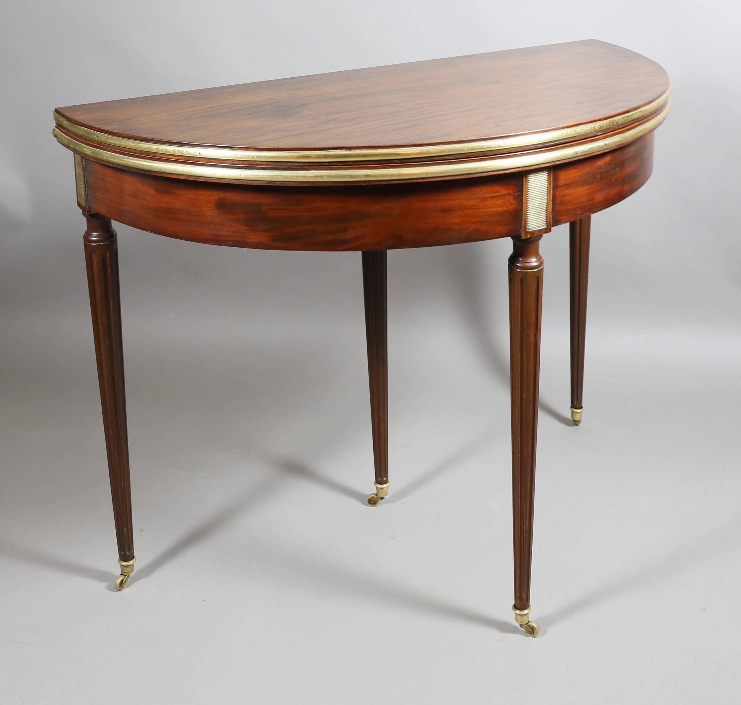 Demilune shape with hinged top opening to a felt lined playing surface over a conforming frieze with circular tapered fluted legs headed by grillwork panels, rear legs pulls out all ending on casters.