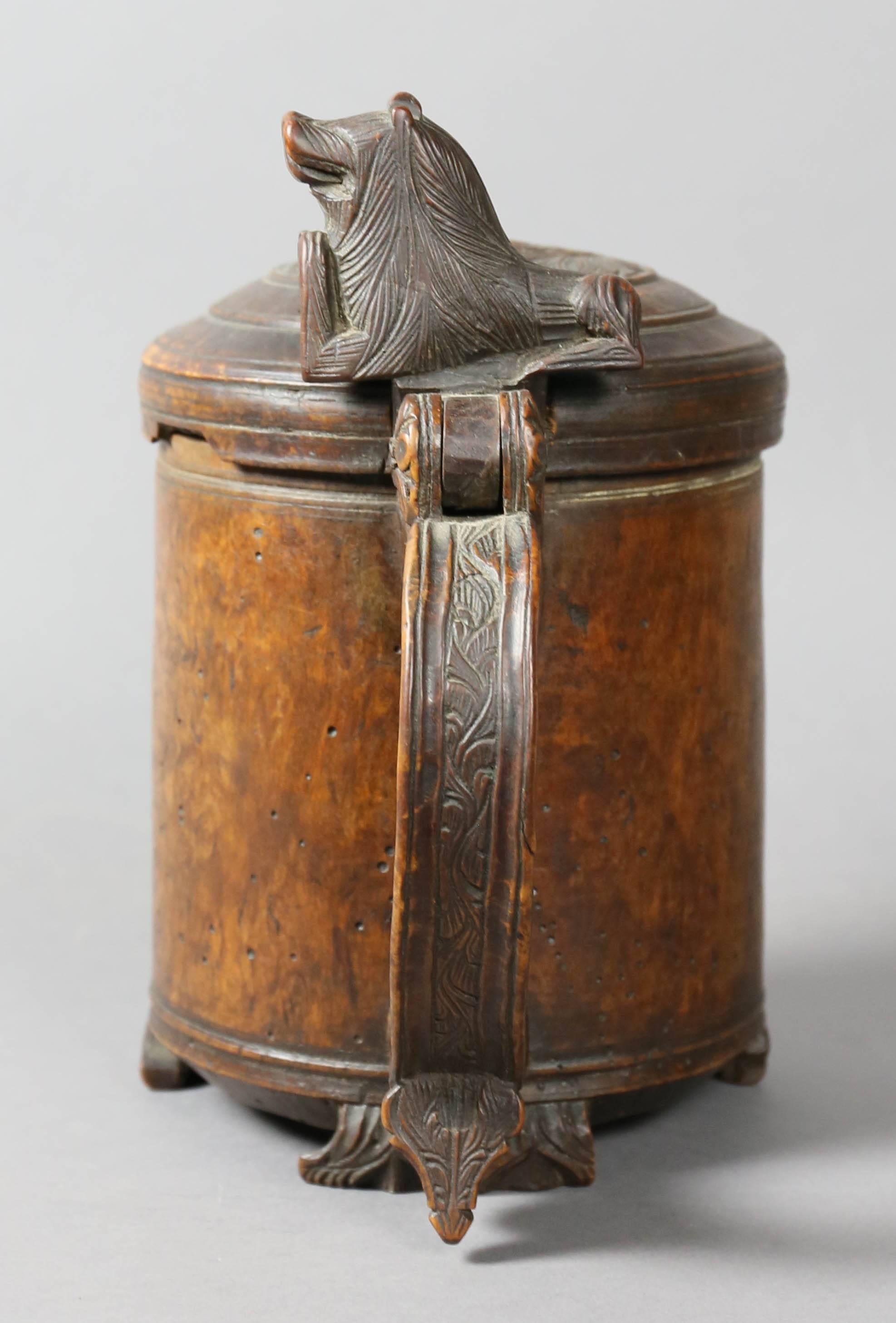 Foliate carved domed hinged lid with figural thumbpiece, cylindrical body with carved feet.