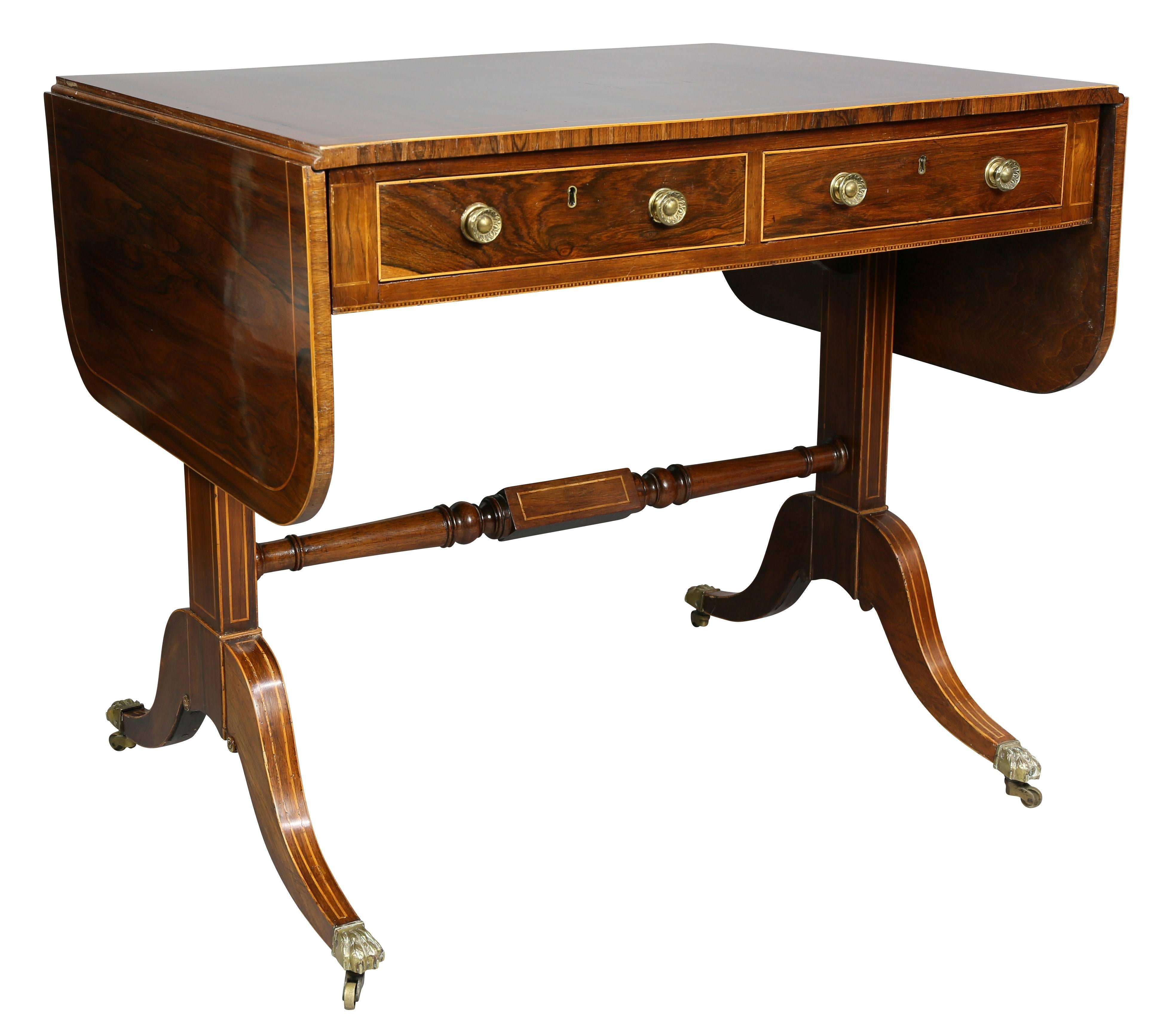 Rectangular top with stringing along edge with drop leaves over a pair of drawers with opposing false drawers raised on a trestle base with turned stretcher, saber legs and casters.