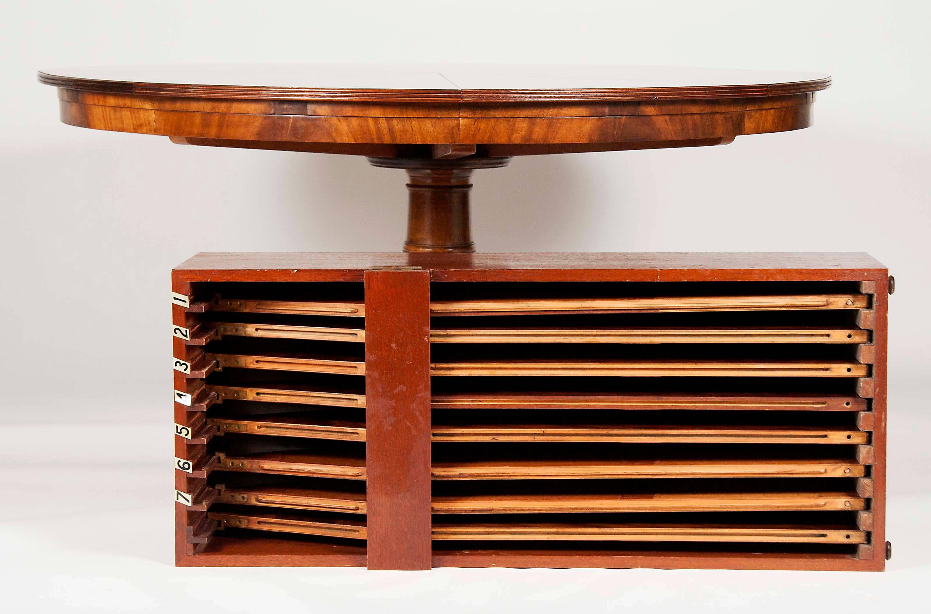 With figured mahogany top with a mechanism where you spin the table and it opens like a kaleidoscope and you insert leaves which enable the table to expand open circular, on a turned support raised on four saber legs ending on brass caps. Includes
