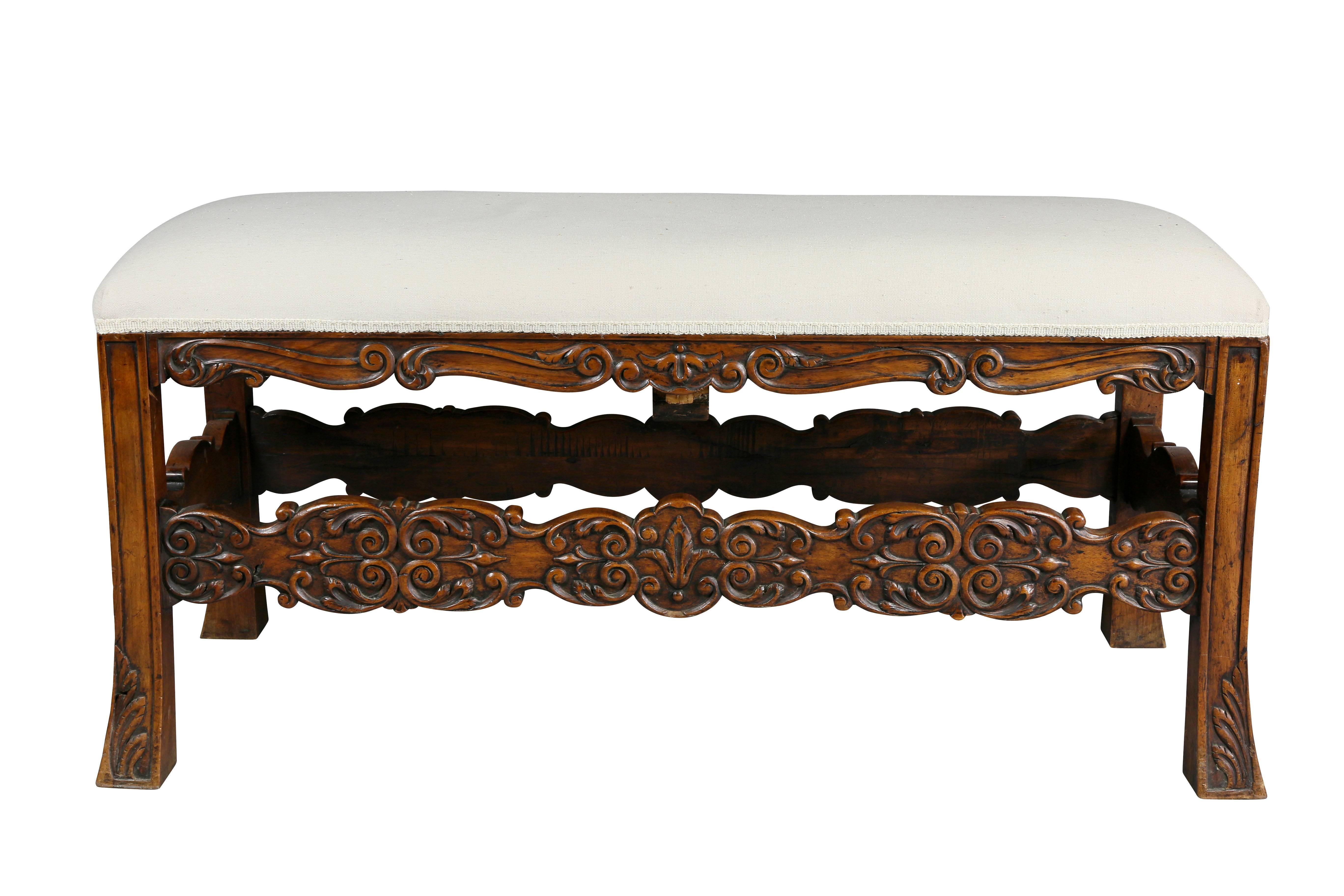 With rectangular upholstered top over a carved frame and carved stretchers ending on slightly flared square legs.