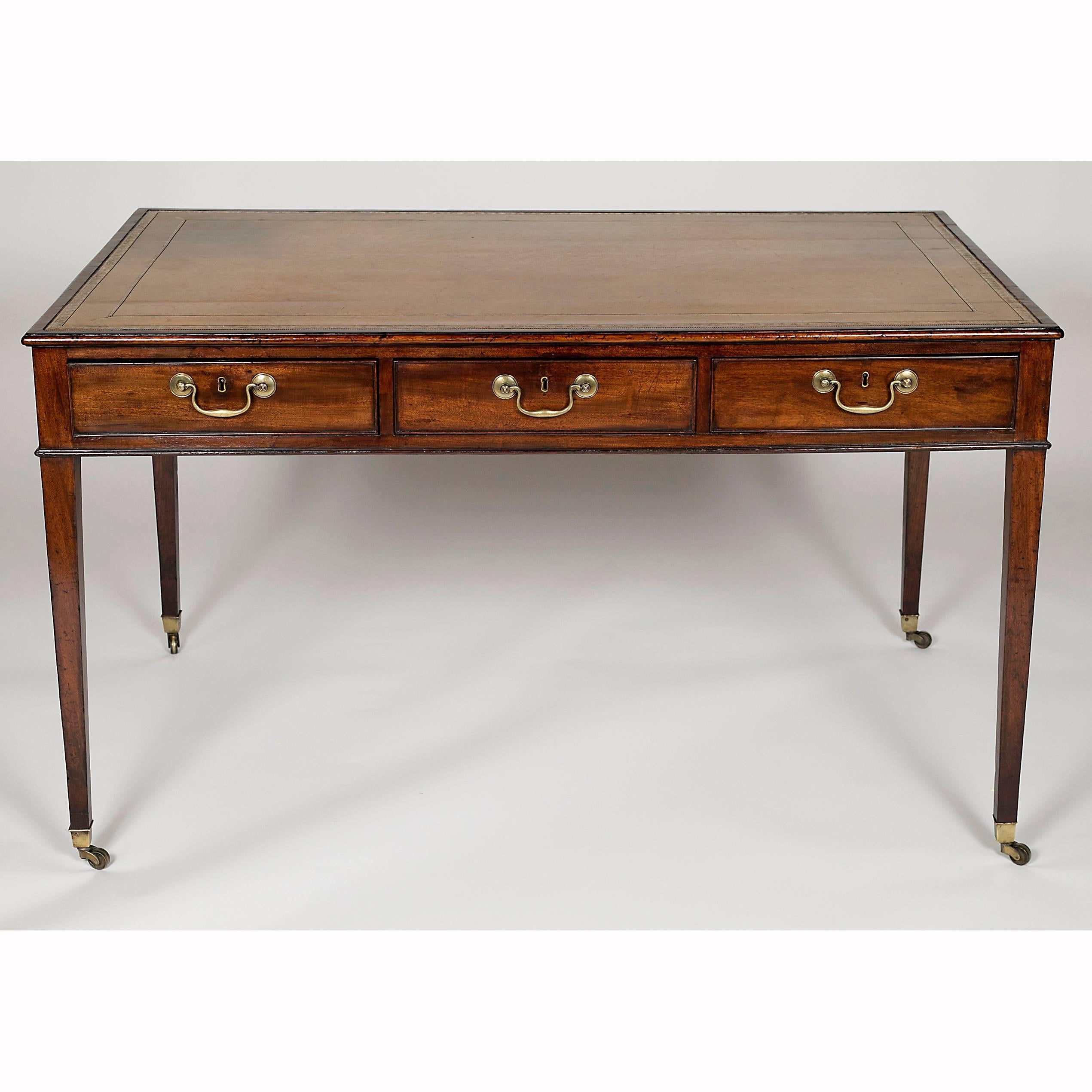 With gold color finely tooled rectangular leather top set in conforming crossbanded top over three drawers with brass bail handles and opposing false drawers raised on square tapered legs ending on brass cup casters.