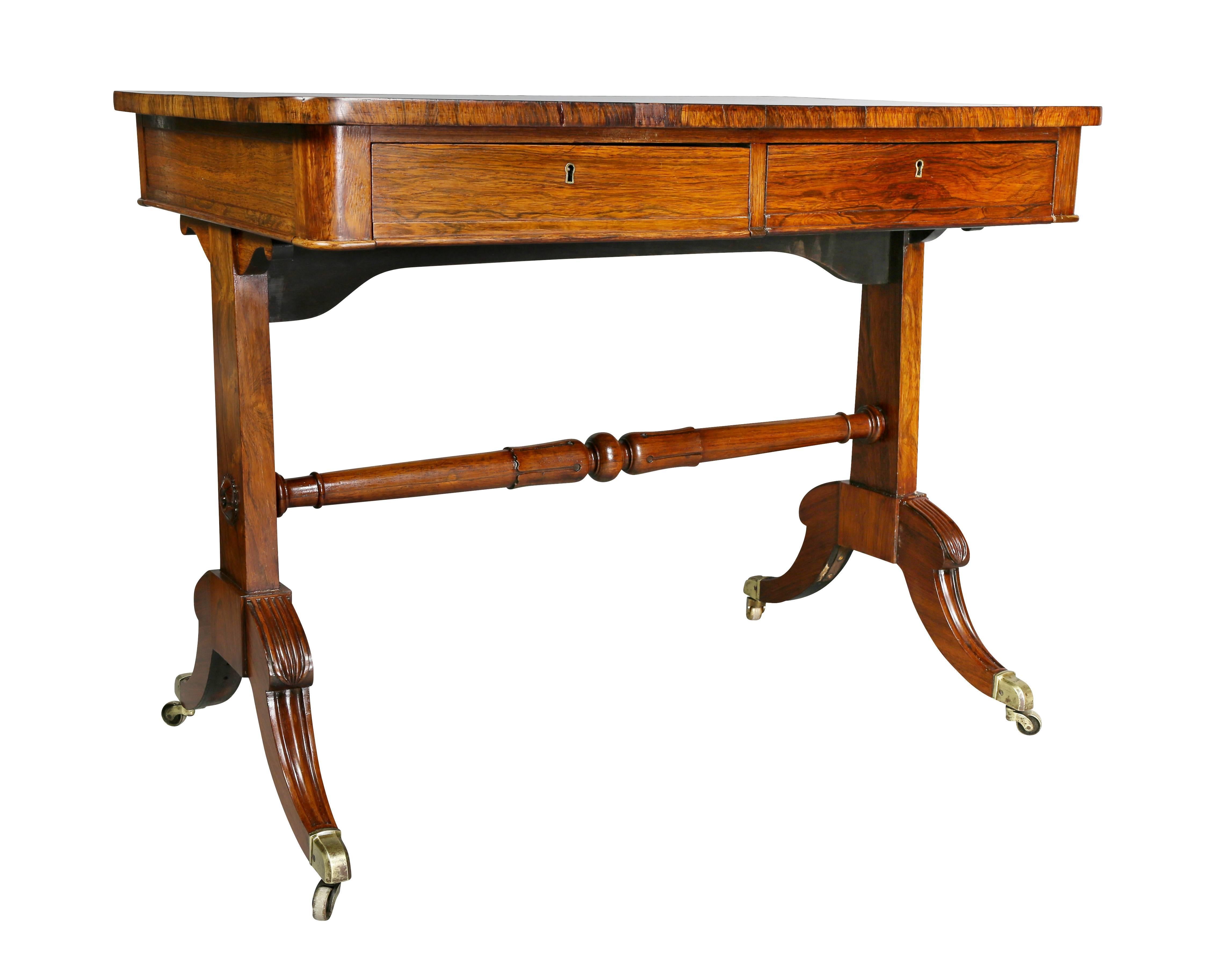 With black inset leather and tooled writing surface over four working drawers  raised on a trestle base with turned stretcher and saber legs and casters.