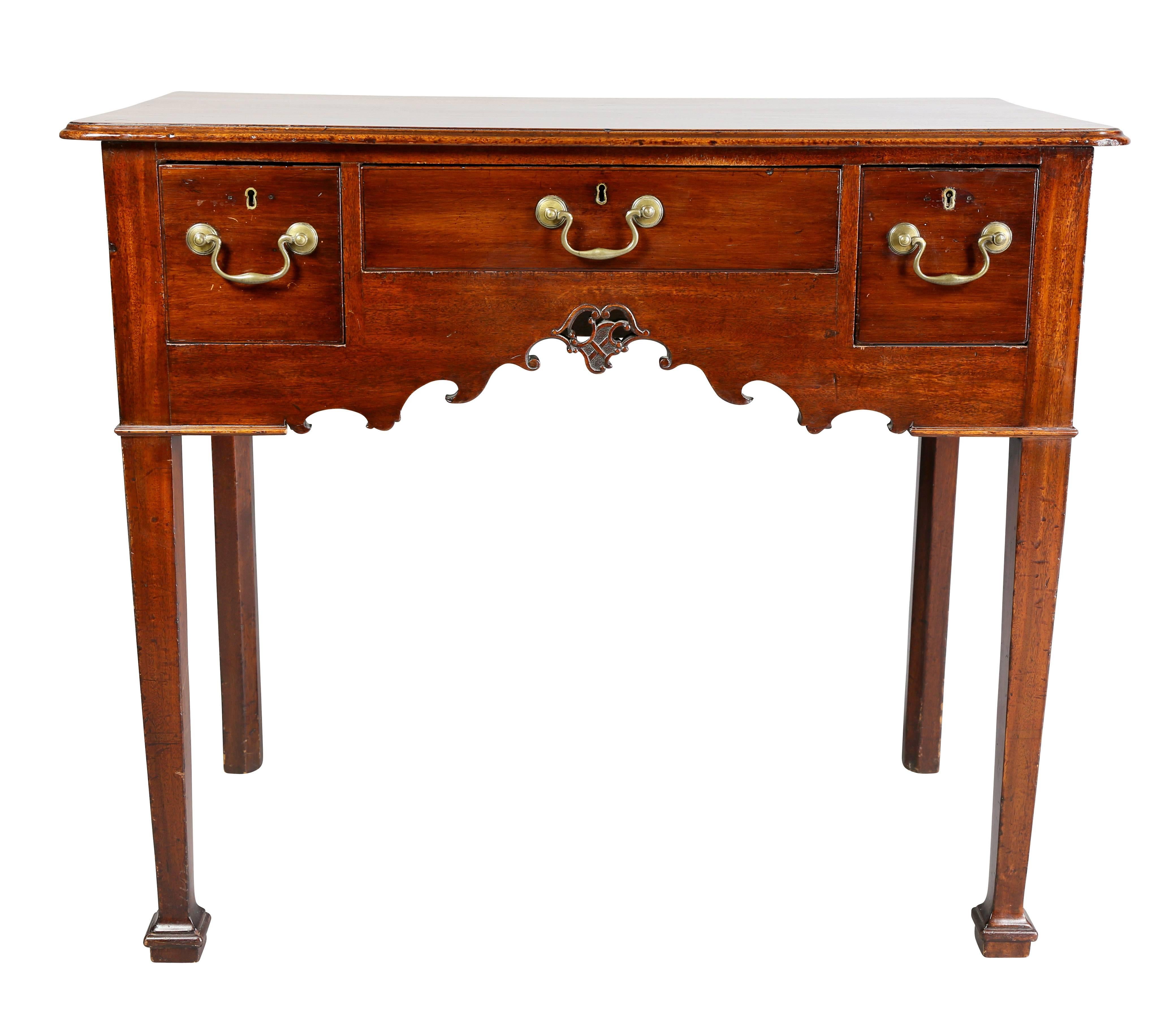 With rectangular top over a long drawer flanked by a single drawer, apron carved with scrolls and central cartouche, raised on square tapered legs, block feet.