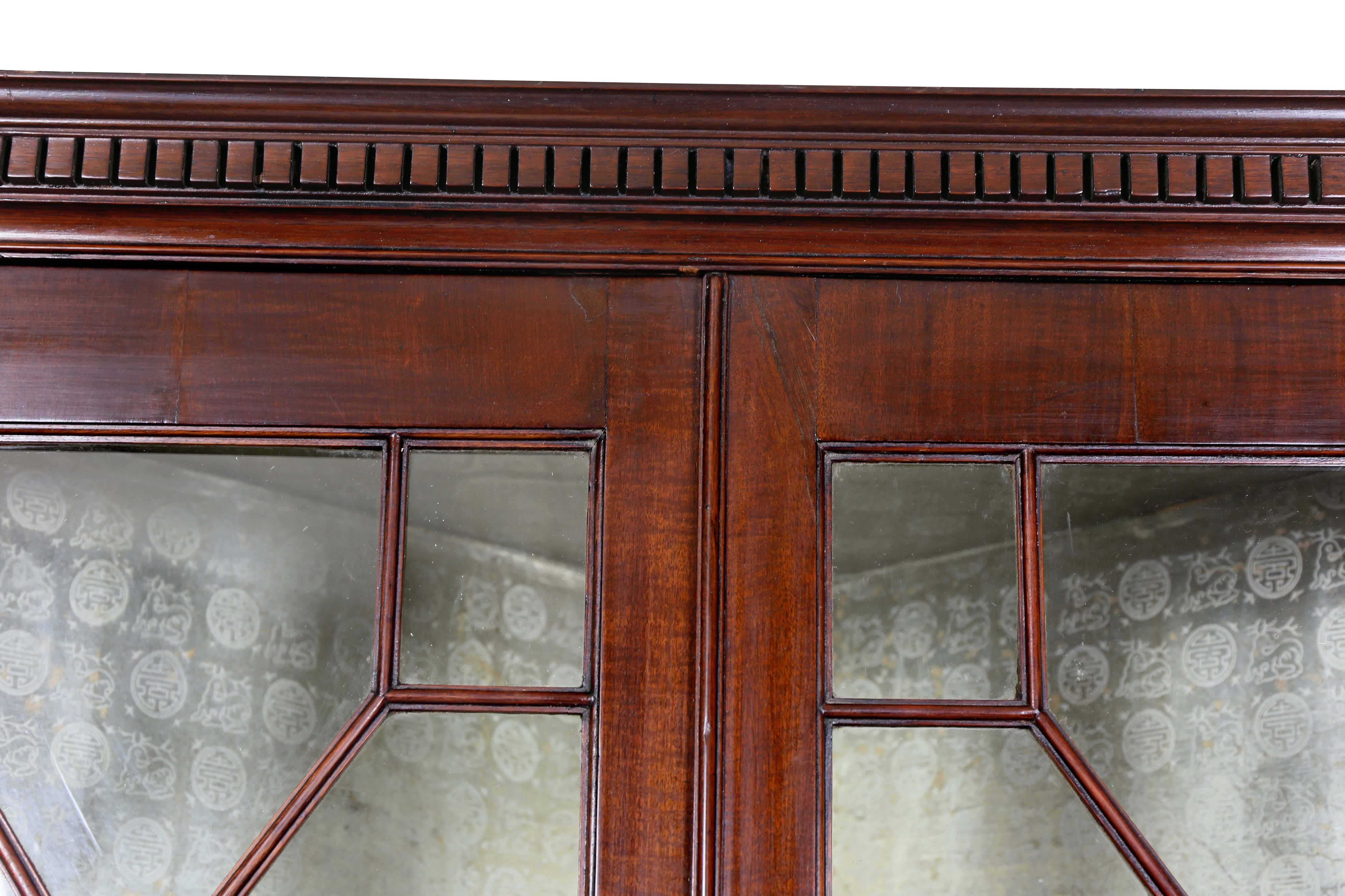 In two parts with a dentilled cornice over a pair of Chinese Chippendale mullioned glazed doors enclosing shelves, the base with a pair of panelled doors and bracket feet.