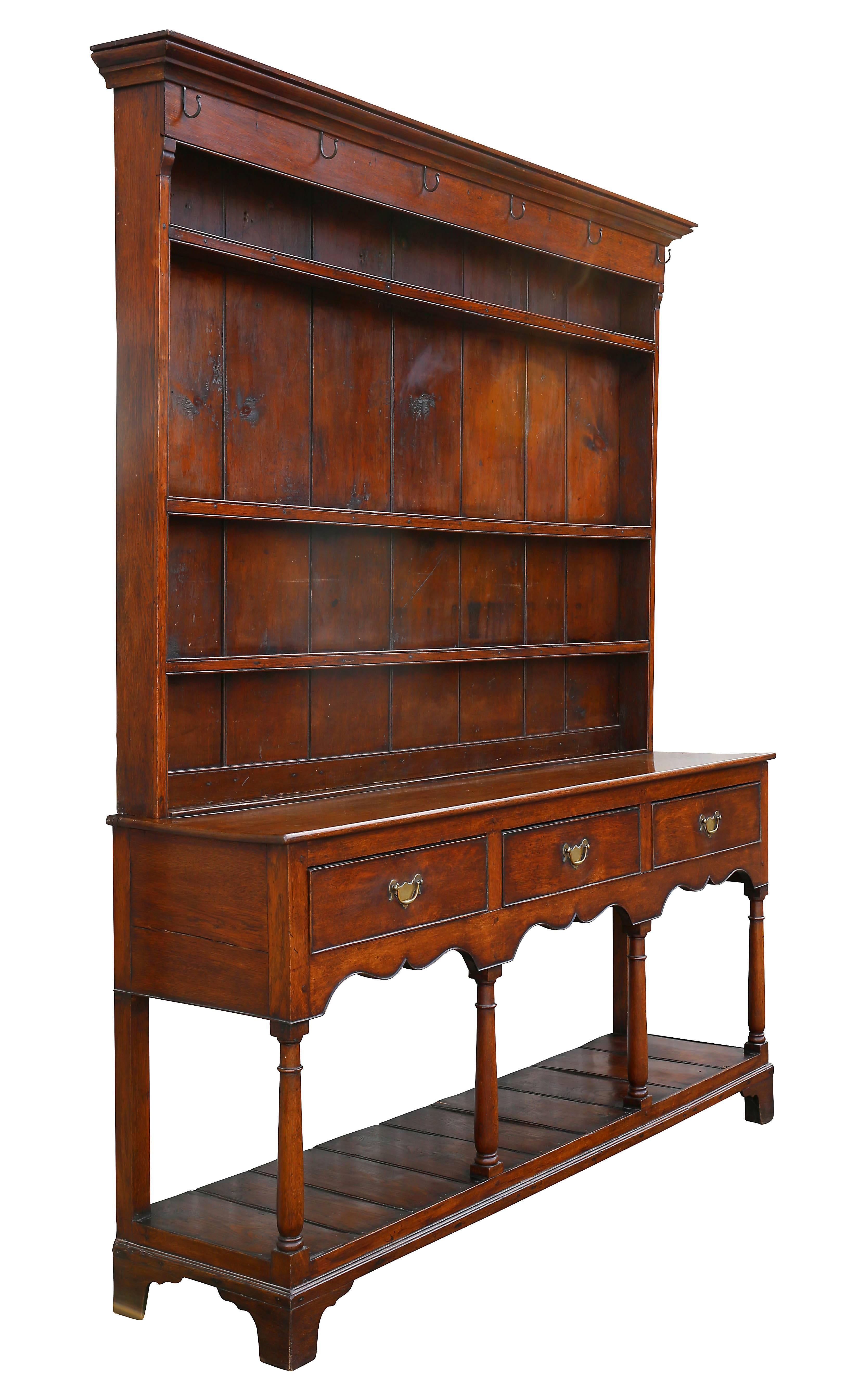 In two parts with molded cornice with cup holder nails above three shelves, the base with three drawers and shaped apron above a lower pot shelf supported with columns, bracket base.