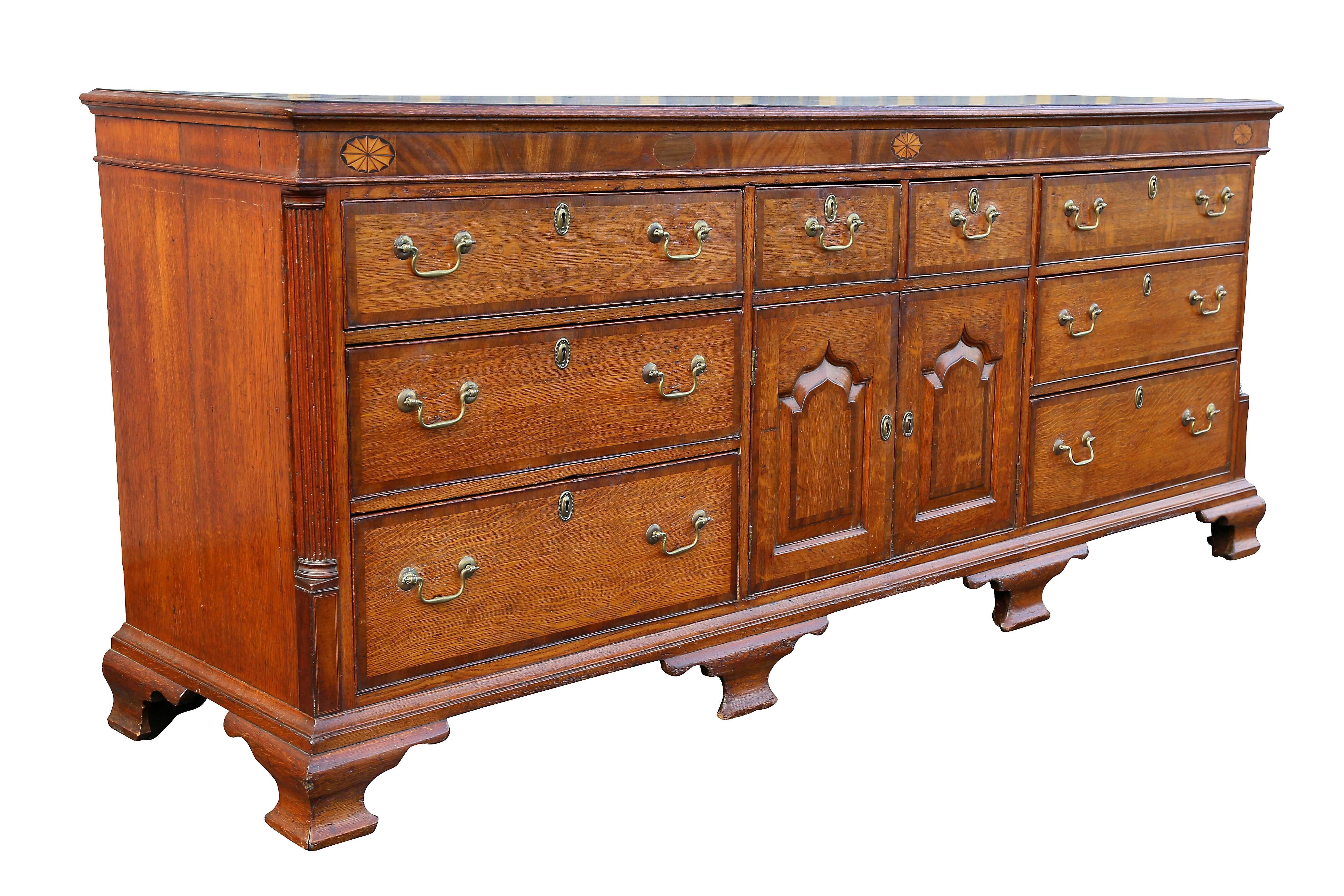 Rectangular top with molded edge over a frieze with paterae inlays, over two small drawers over a pair of panelled cabinet doors flanked by three graduated drawers, all within fluted quarter columns, raised on ogee bracket feet.