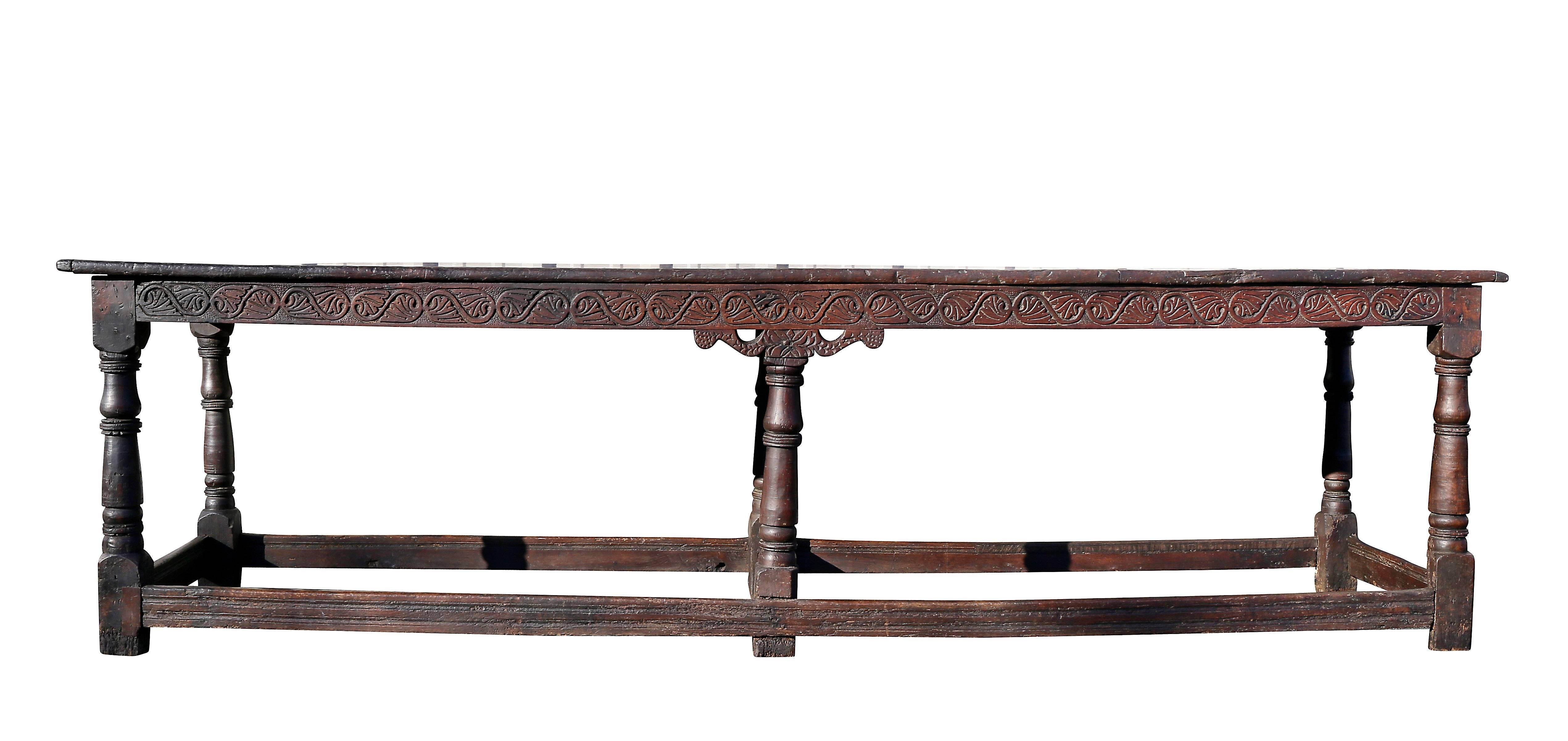 With plank board top with battened ends over a frieze carved with stylized leaves and raised on six turned legs joined by a box stretcher. Back with horizontal carved and molded design. Slight reduction in length from original size.