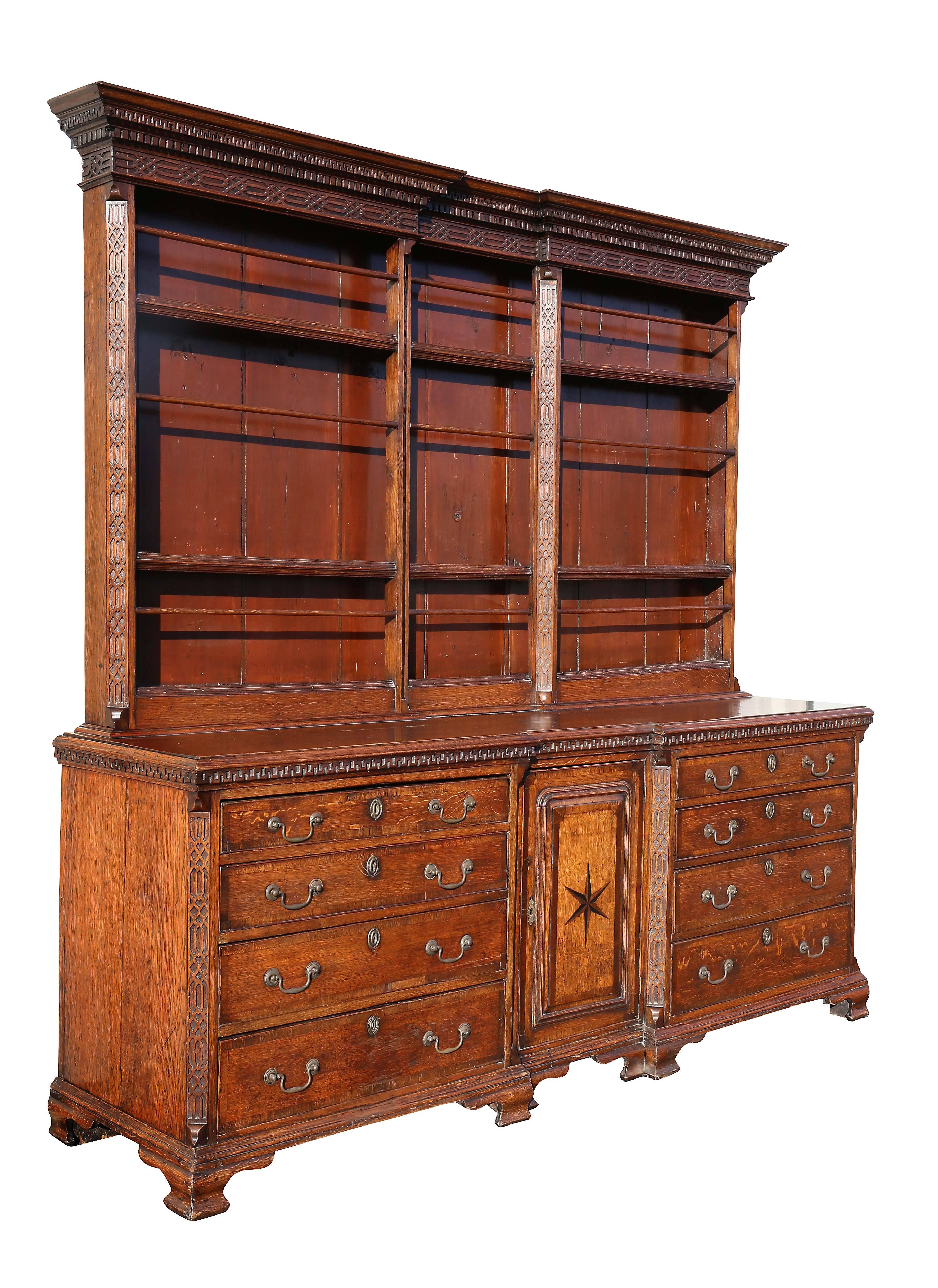 With shaped breakfront cornice with dentilled and Greek key decoration over blind fret Chippendale frieze all-over shelves, the conforming base with central door with star inlay flanked by four drawers and raised on ogee bracket feet. Brass bail