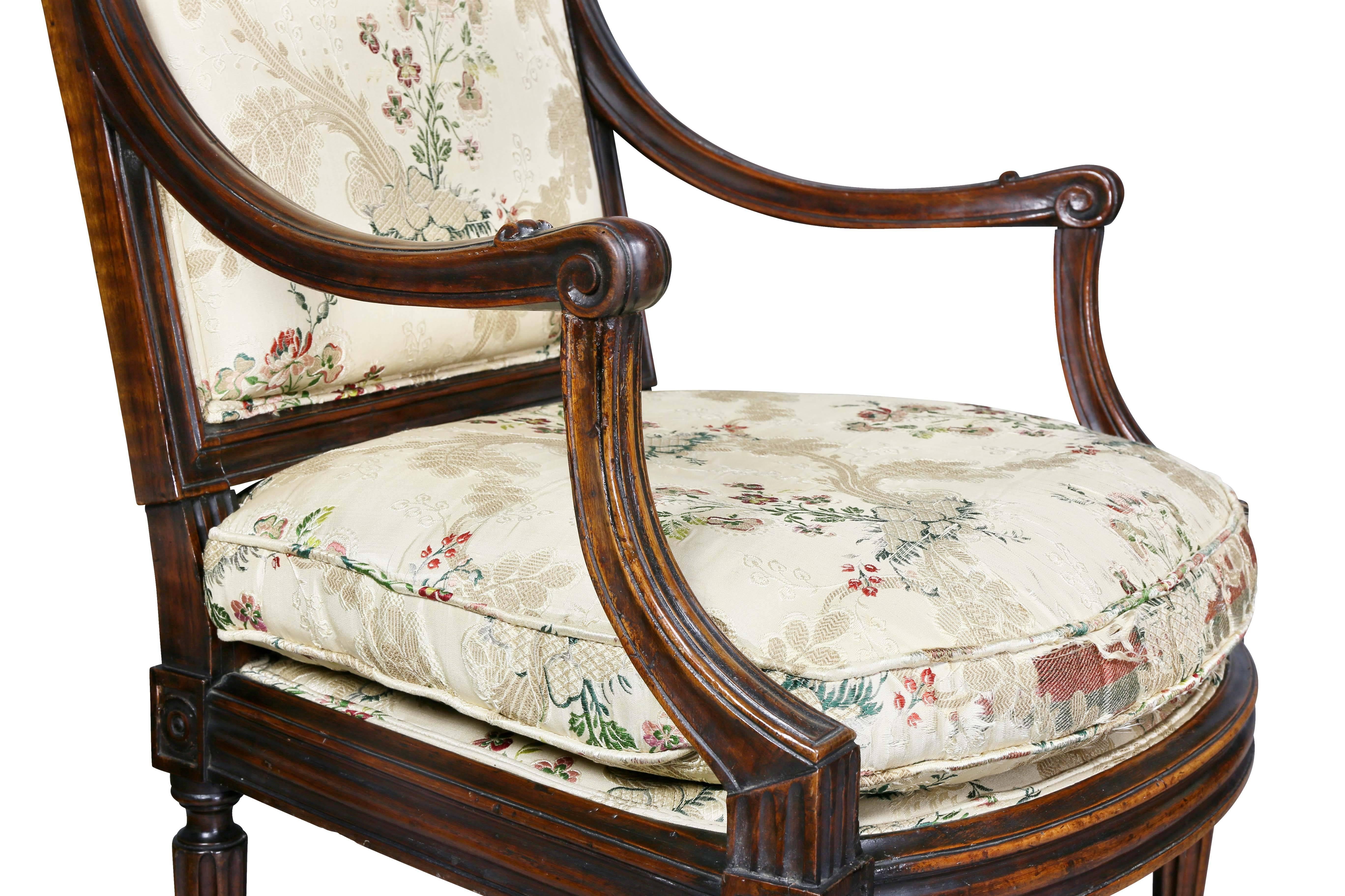 Each with an arched simply carved upholstered back and seat and downswept arms with scroll carved handholds, raised on circular tapered fluted legs headed by roundels.