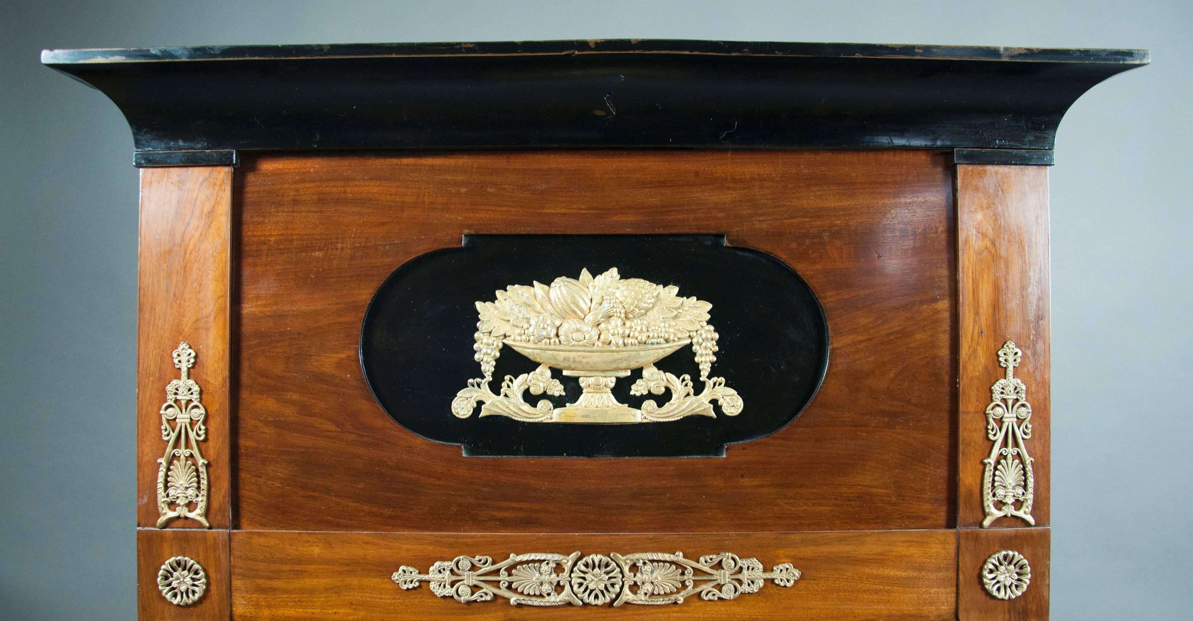 Rectangular with ebonized cornice over a panel with central cornucopia over a mirror plate with a conforming bronze mounted frame. Frame flanked with pair of candleholders.