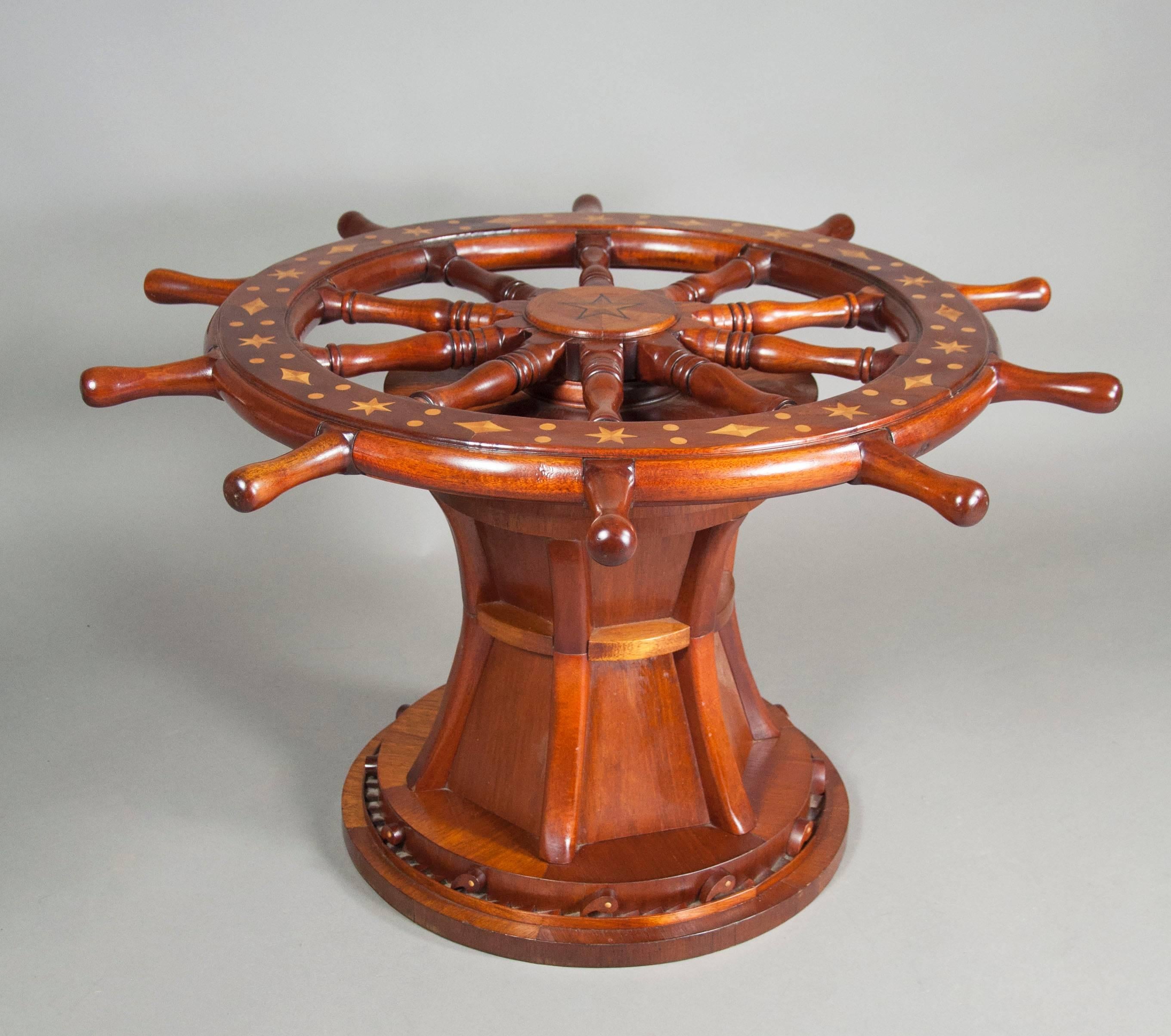 With glass top over an inlaid spoked ships wheel with winch form support and circular base with ratcheted and spring mounted locking tabs.