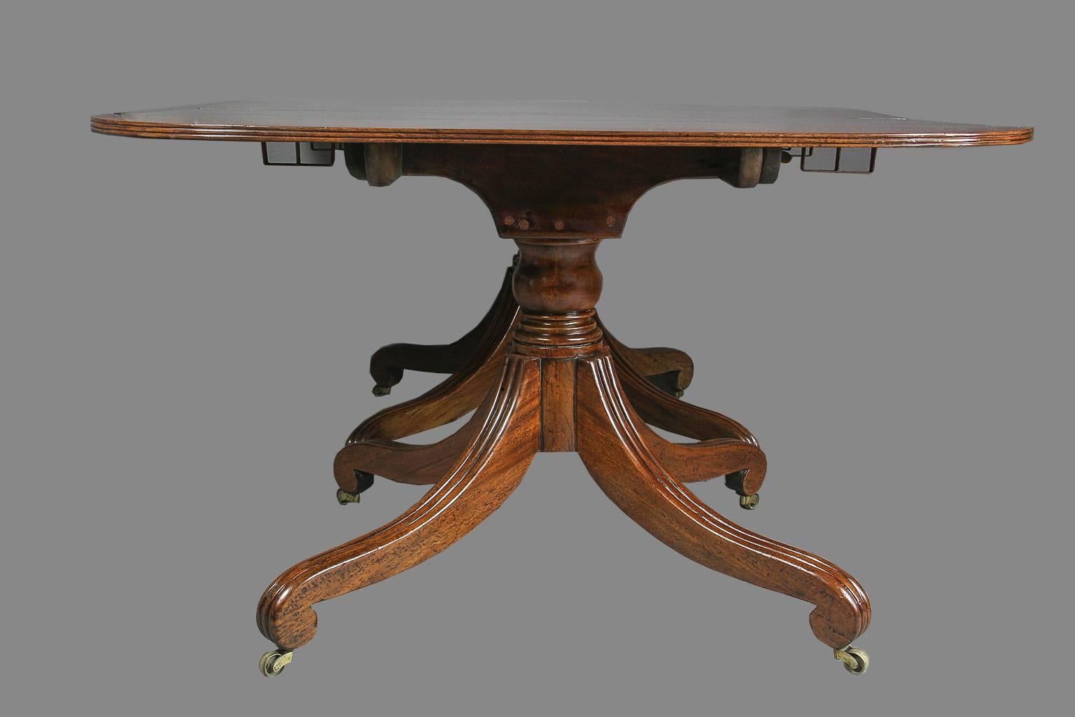 Beautiful figured three-section top with two additional original leaves supported on three urn form pillars each joined by four reeded saber legs with scroll feet and casters. Table has clips and wood runners.