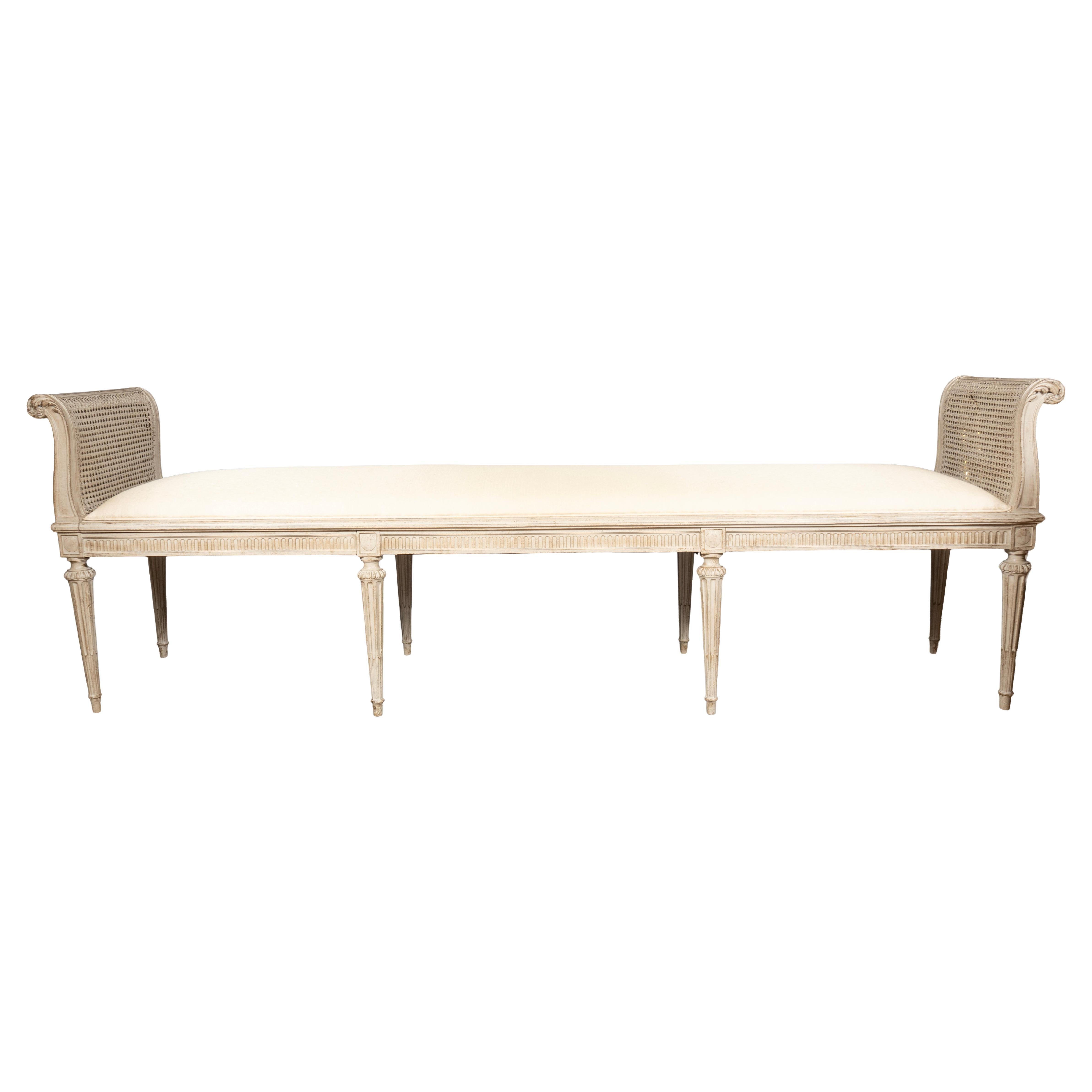 Rectangulaire avec des extrémités sculptées en relief et à volutes, avec cannelures. Assise tapissée et barre d'assise sculptée en cannelure, pieds circulaires fuselés et cannelés.