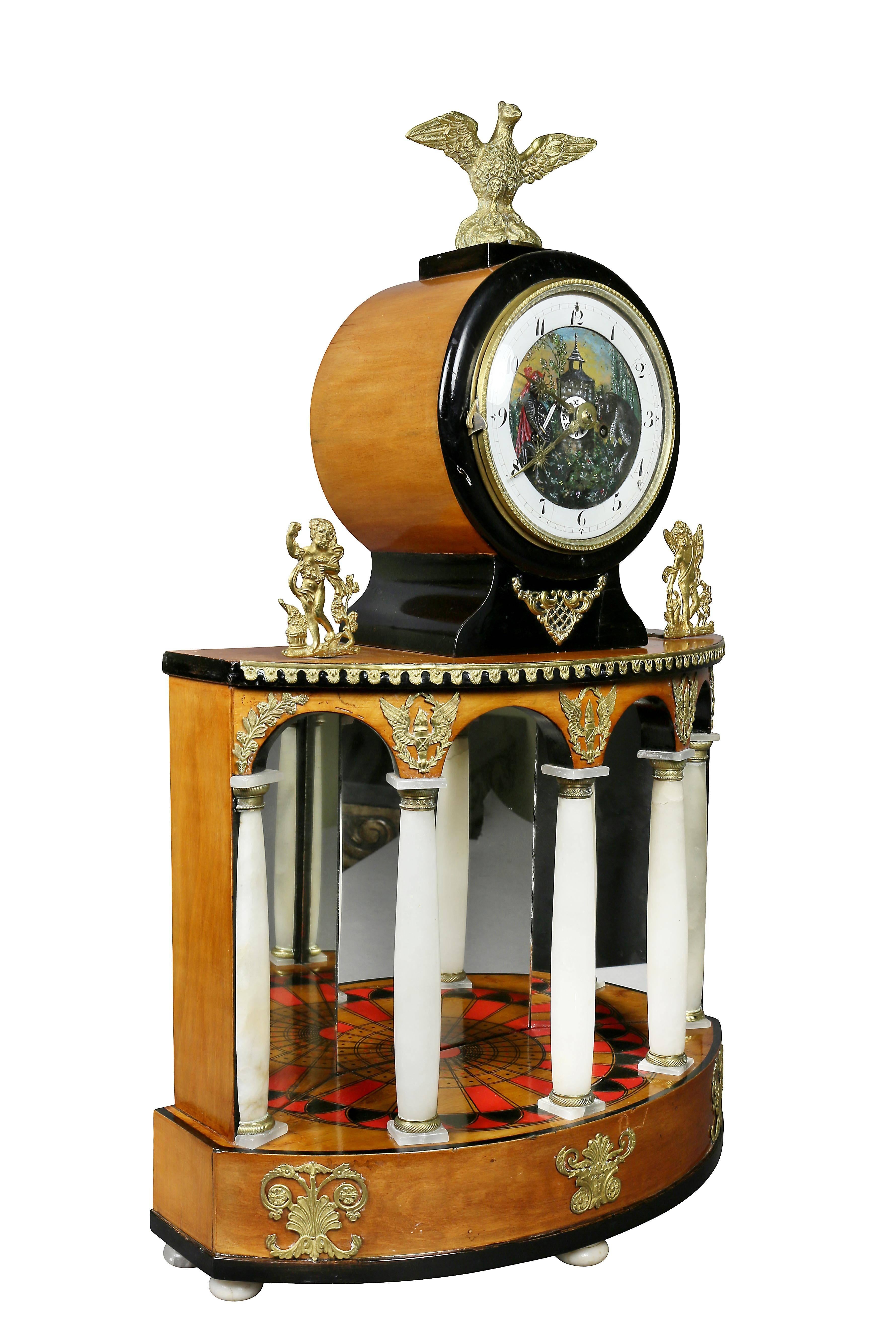 With eagle finial over an enameled and painted clock face over an inlaid portico with mirror back and alabaster columns on a plinth base.