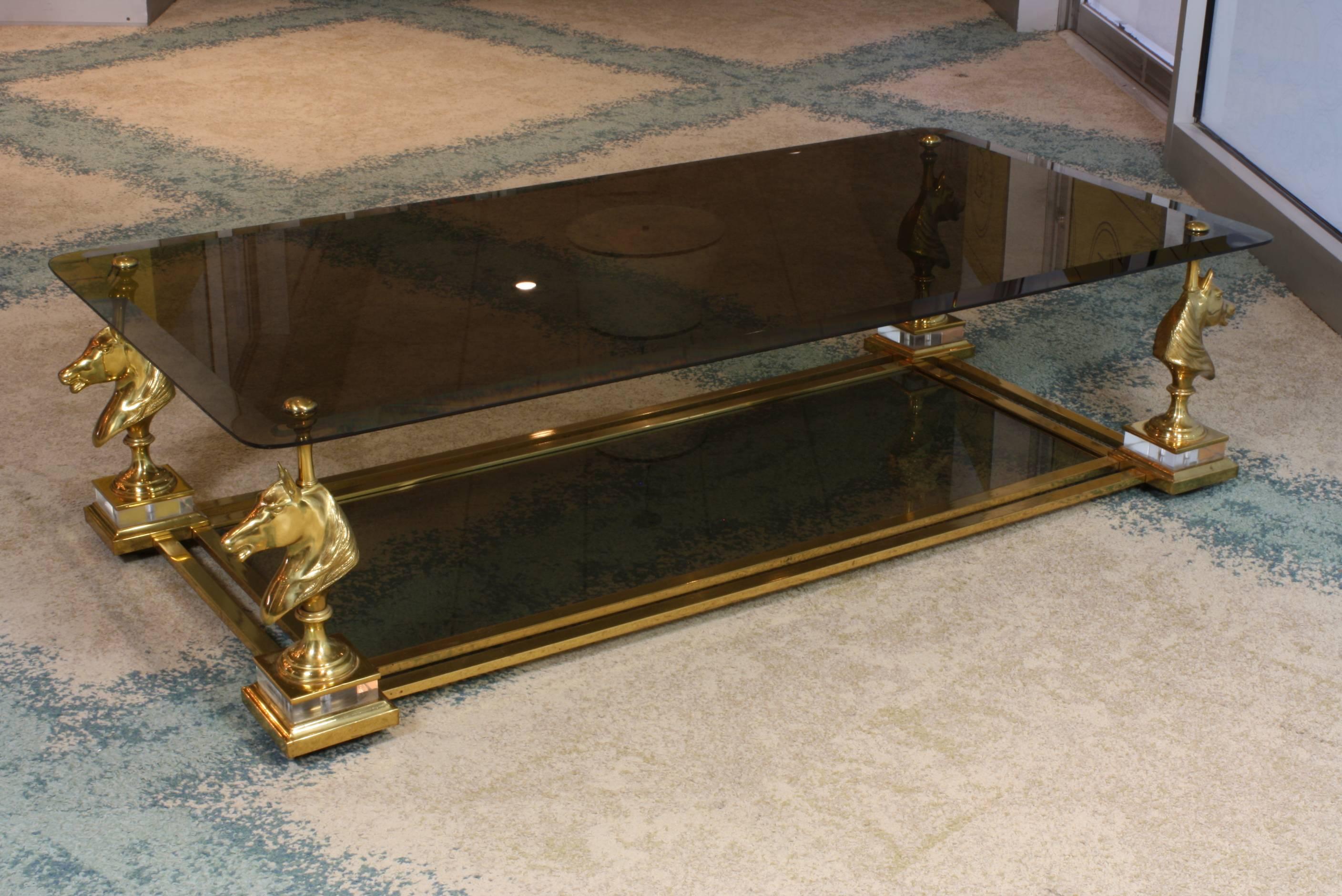 Large size French gilded bronze, brass and smokey glass two-tiered coffee table by Maison Charles (mid-20th century.) The horse heads rest on clear Lucite plinths, with double stretchers connecting them and supporting the lower glass tier. The top