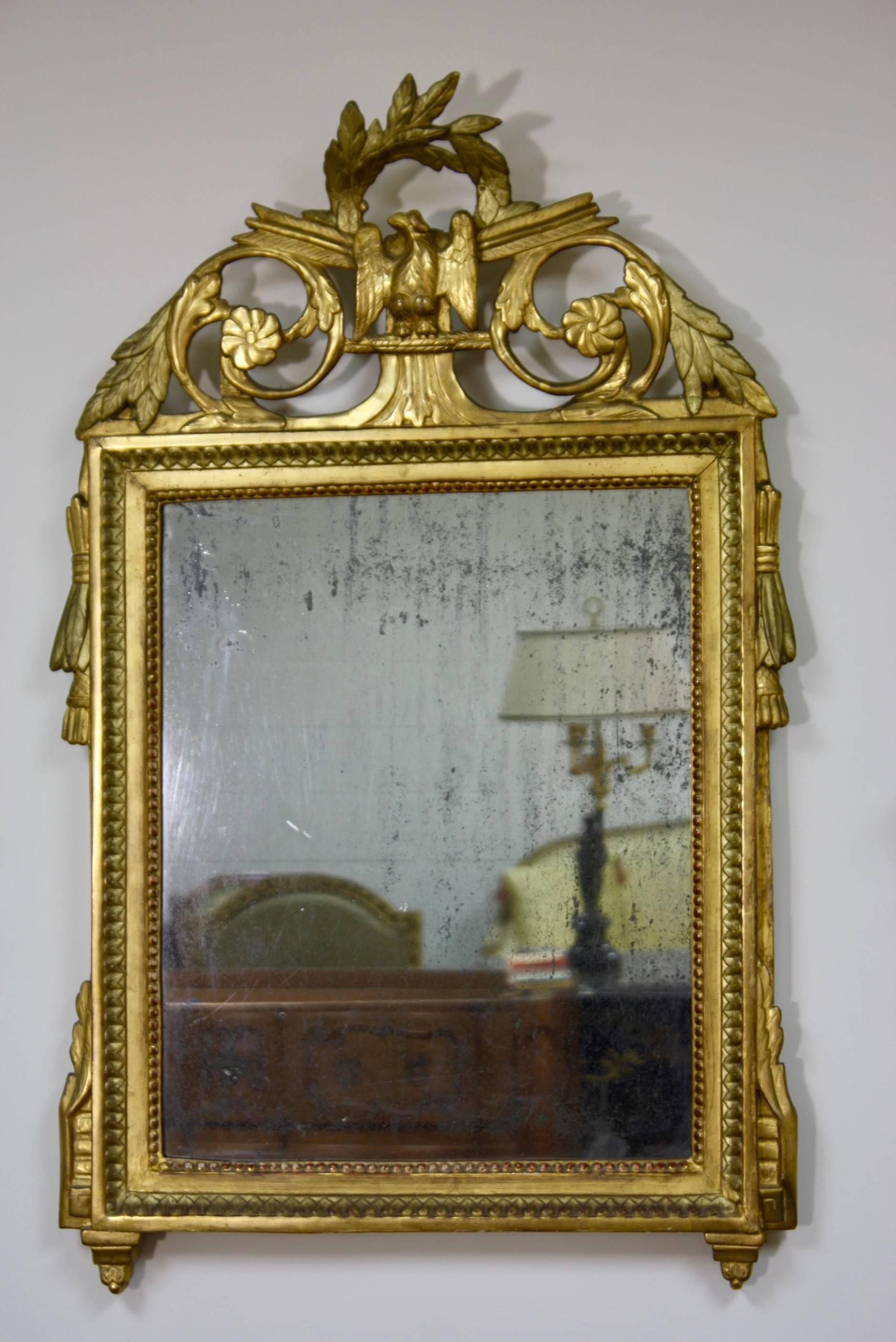 Miroir trumeau en bois doré d'époque Louis XVI, vers 1780, avec des détails néoclassiques, dont une couronne de laurier et un aigle sur le cartouche, verre au mercure d'origine et dossier en bois.