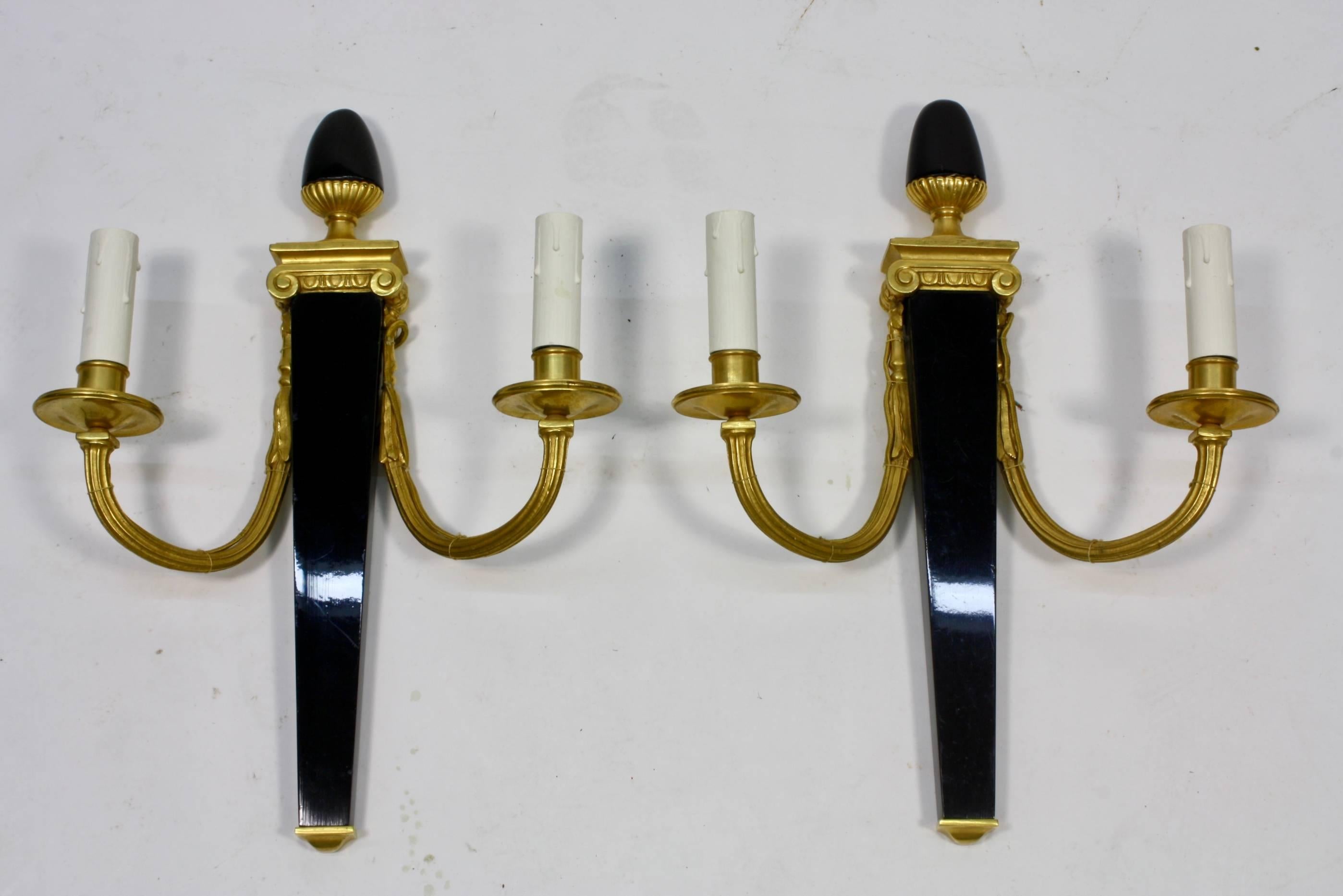 A set of four neoclassical sconces by the French manufacturer Maison Bagues. Each sconces features a black-lacquered body tapering to a gilt bronze base with an egg-from finial. The two fluted gilt bronze arms attach to an ionic style capital. Each