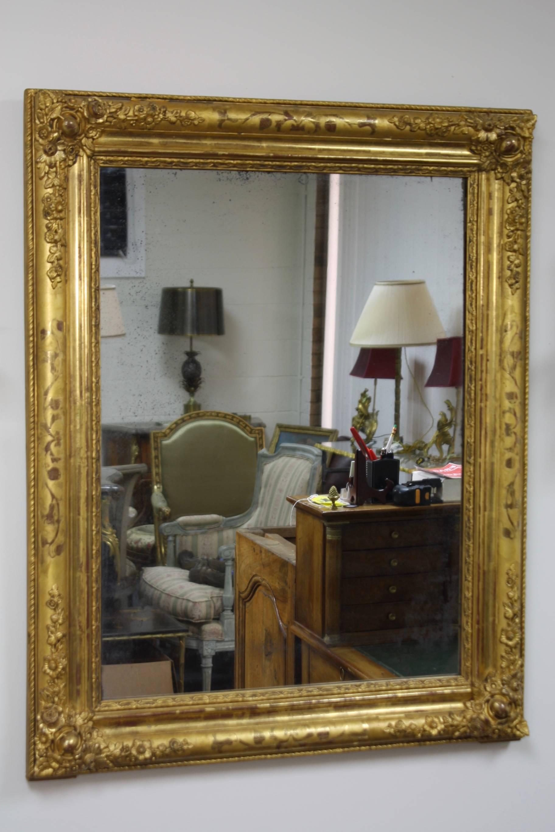 Beautiful French giltwood mirror from the Charles X period, (circa 1830). The mirror features carved floral details in the corners and vine design on the sides. Nice old mercury glass shows its age and could be original. The mirror has an old wood