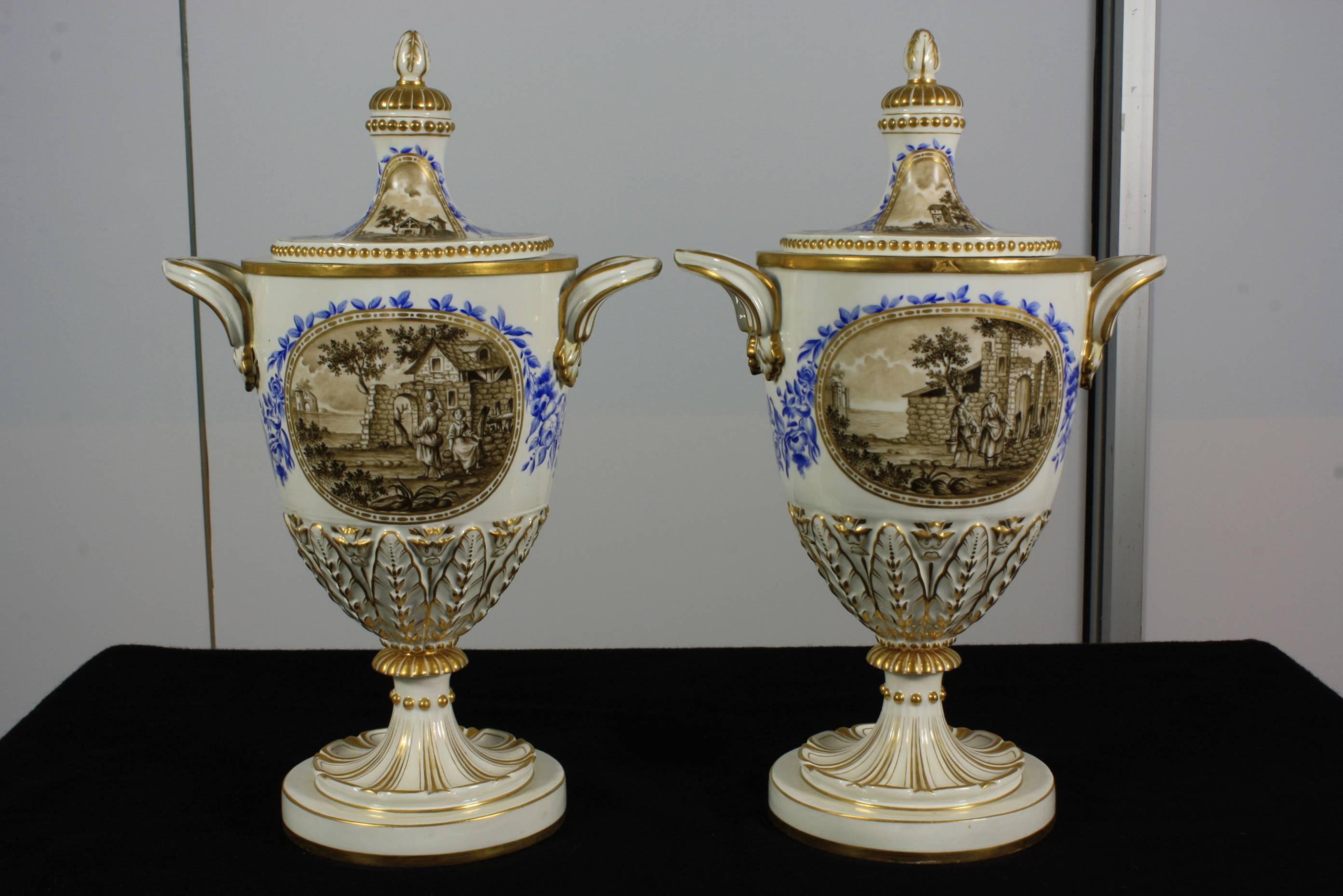 Pair of elegant 19th century Italian porcelain lidded urns with hand-painted scenes and gilded details. One side of the urns features a neoclassical scene, and the reverse side features a bucolic scene. Each of the painted scenes is framed by a
