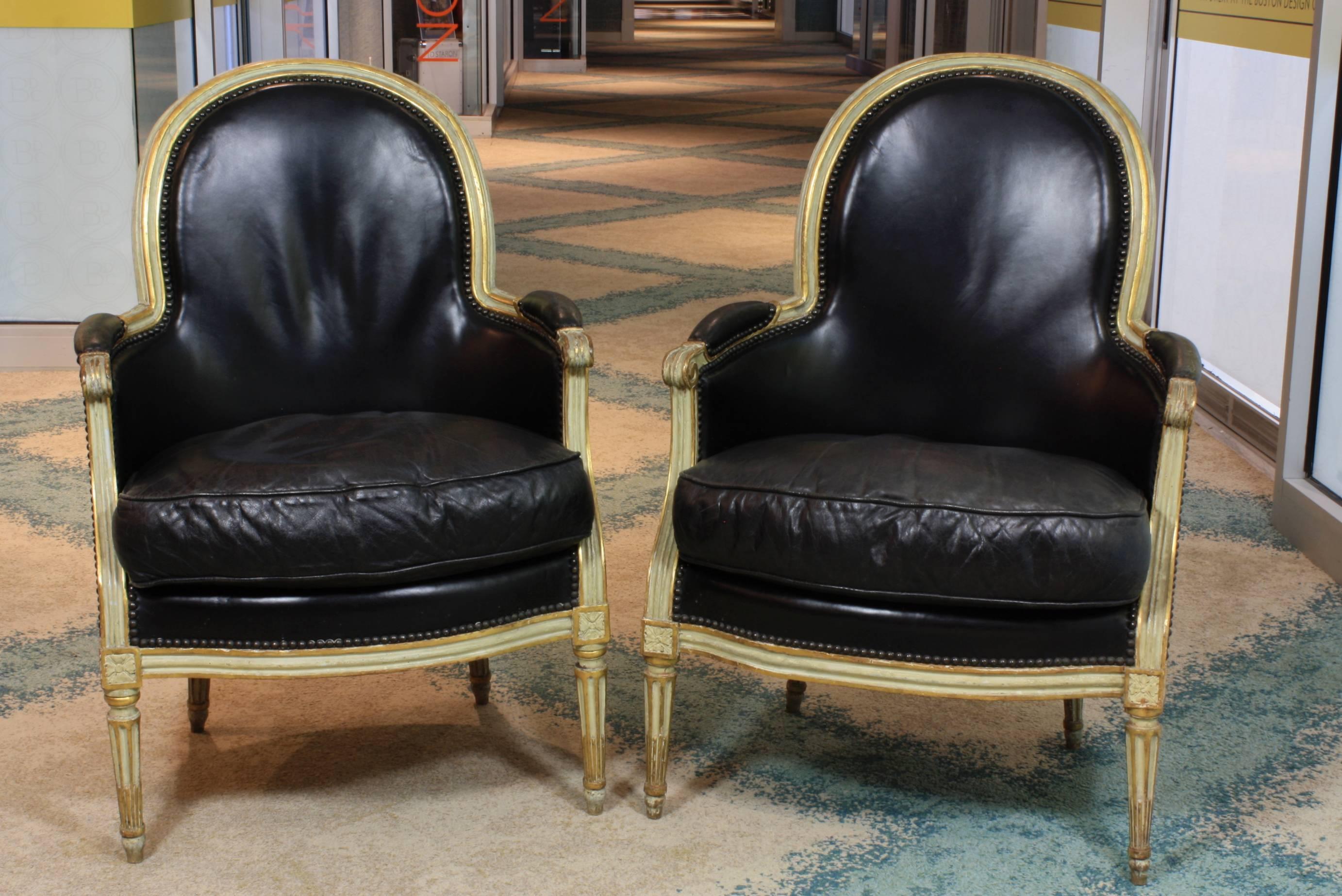 Pair of French Louis XVI period bergeres upholstered in more recent black leather finished with brass nailhead trim, circa 1785. The frames are painted in French grey-green (traces of older paint are also seen underneath more recent paint) with