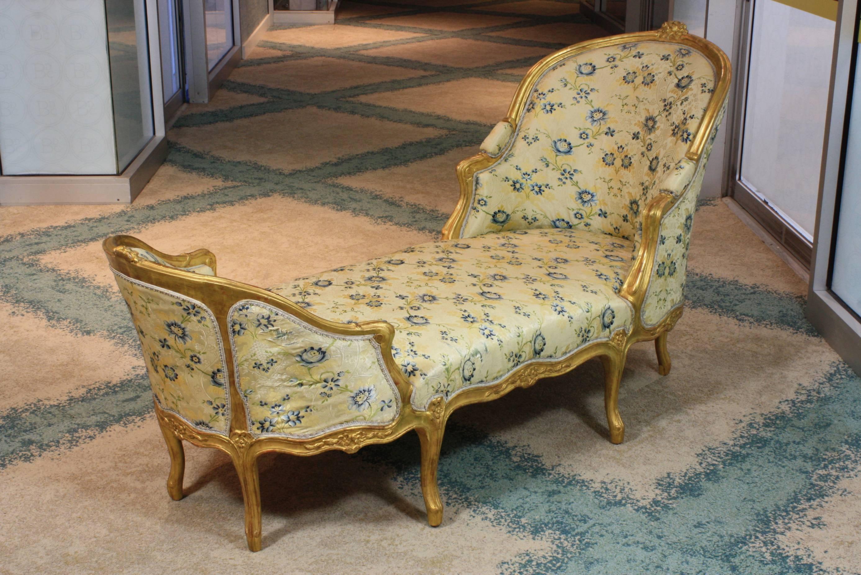 Elegant French Louis XV style giltwood chaise longue, with nicely-carved flower cartouches on the head and foot, floral carvings on the seat rail and other rococo ornaments. Upholstered in lovely silk lampas fabric (probably Tassinari) with gimp