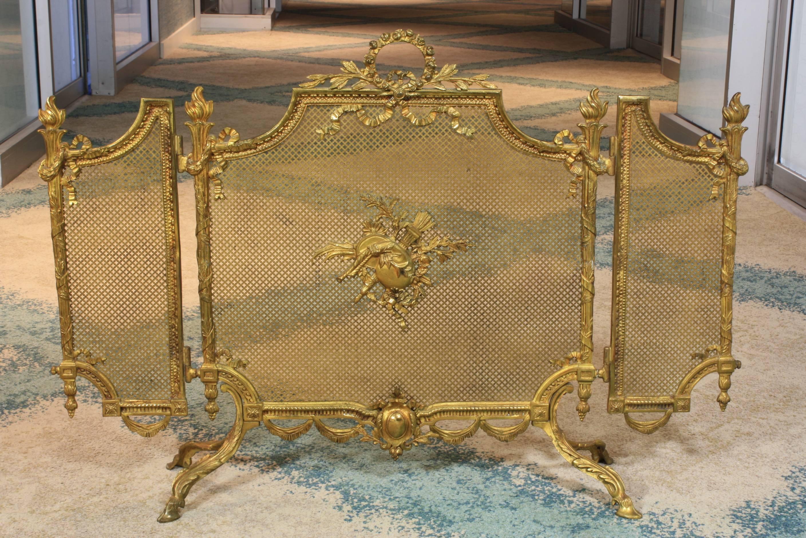 French Louis XVI style gilt bronze fire screen with side panels (19th century). The side panels can swivel backwards to accommodate a range of chimney widths. The fire screen is decorated with typical Louis XVI ornamentation, including a floral