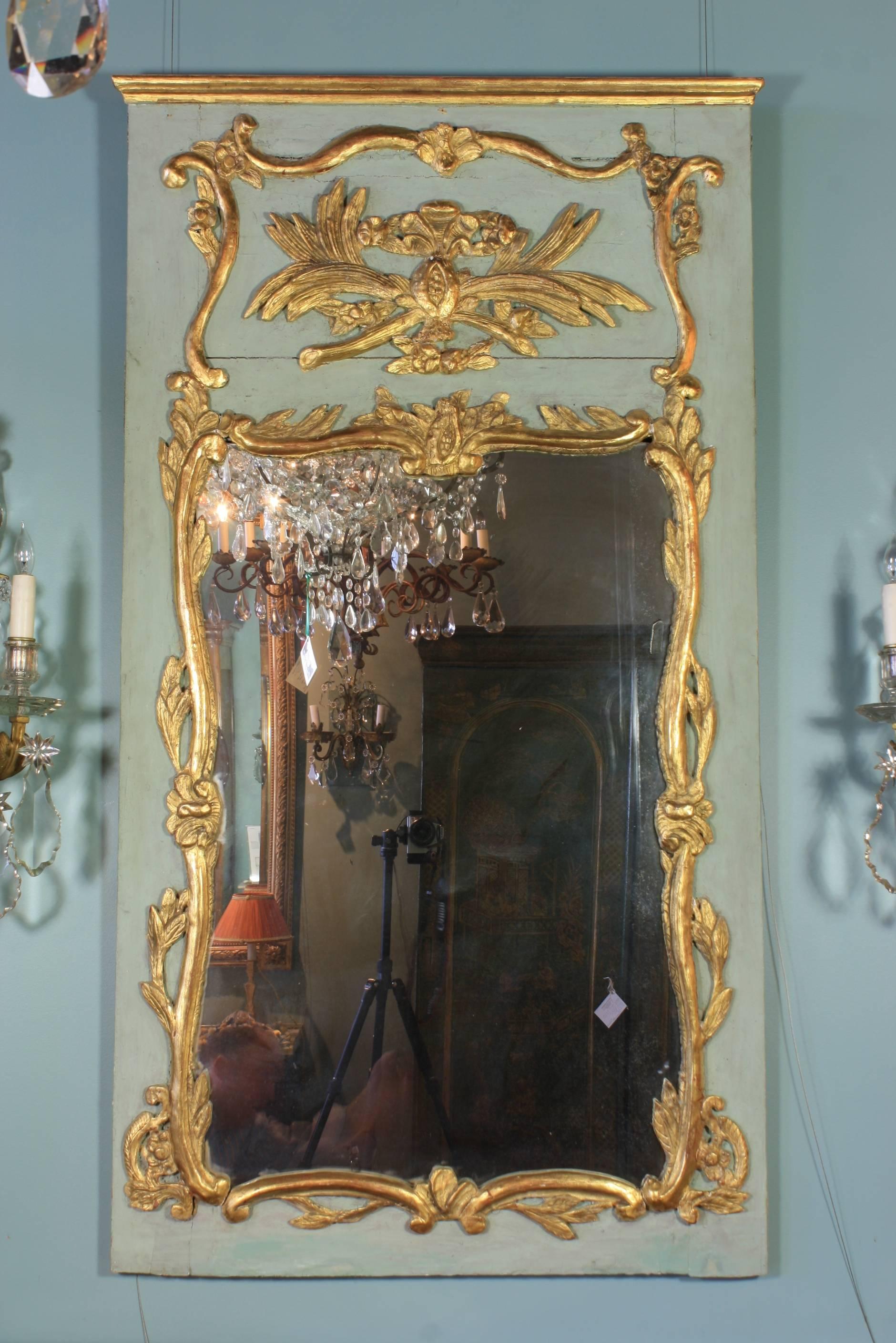 Miroir trumeau français d'époque Louis XV (vers 1750) provenant de Normandie, peint et doré à la feuille avec des grenades stylisées, des volutes, des fleurs, des feuilles et autres ornements rococo. Le verre du miroir est ancien et le miroir a un