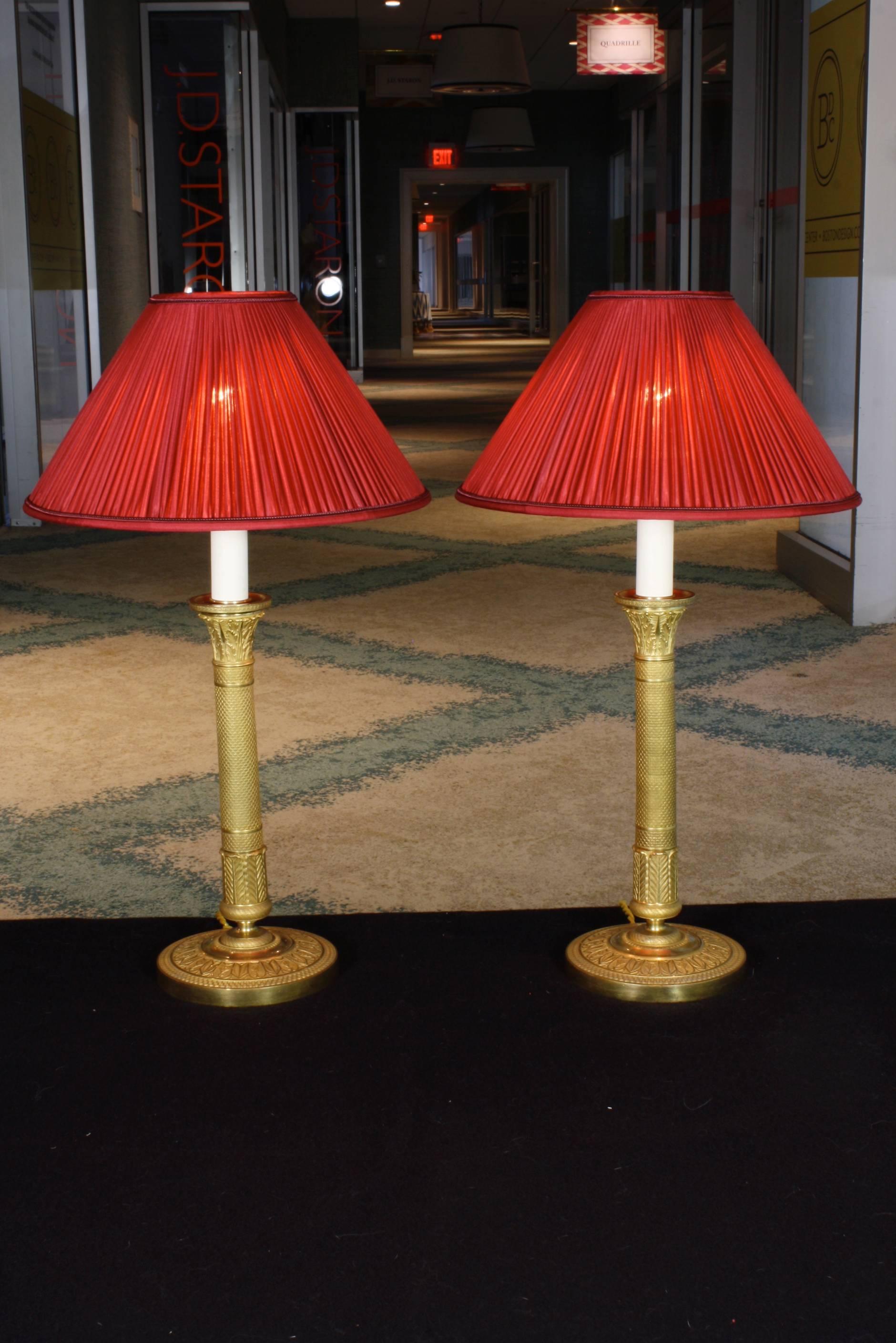 Pair of gilt bronze French Empire style candlesticks that have been retrofitted as lamps with pleated silk shades (late 19th century). The candlesticks are high-quality, finely-chased. Wired for the US, with the wires running through the candlestick