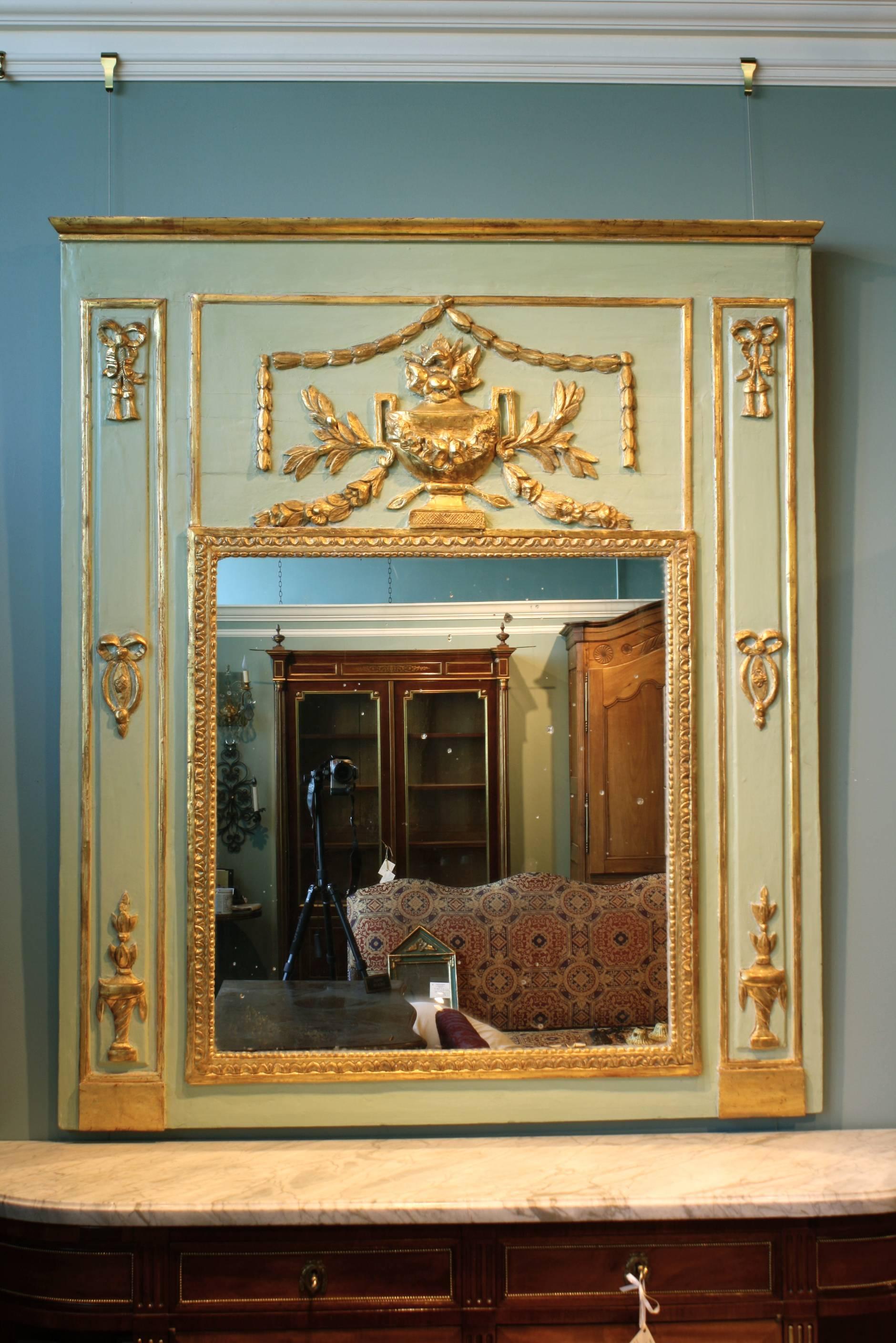 A large scale French Louis XVI period trumeau mirror, with neoclassical detailing, including a large urn with swags and acanthus boughs, bows and smaller urns decorating the sides. The mercury glass appears to be original, and the trumeau has an old
