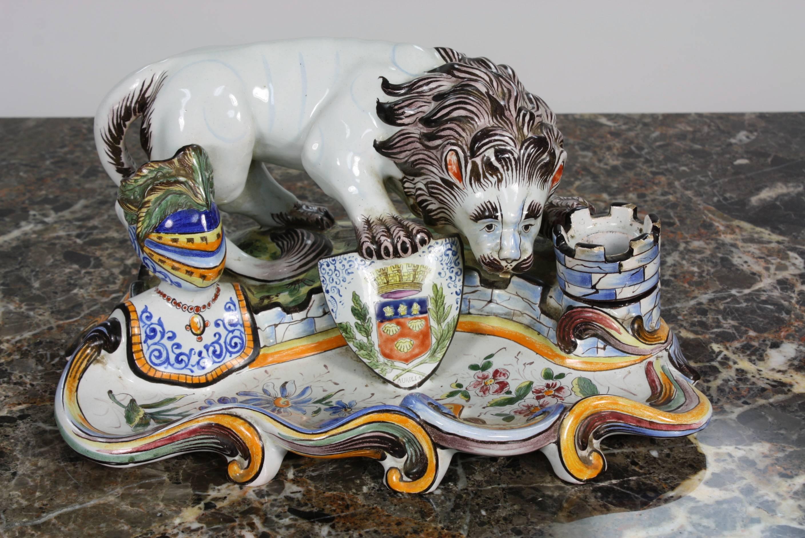 An unusual and highly-decorative 19th century French faience inkwell from Normandy, featuring a stylized lion holding a shield with coat of arms, surrounded by a helmet (hollow for holding pens), and a removable castle inkwell. Underneath marked and
