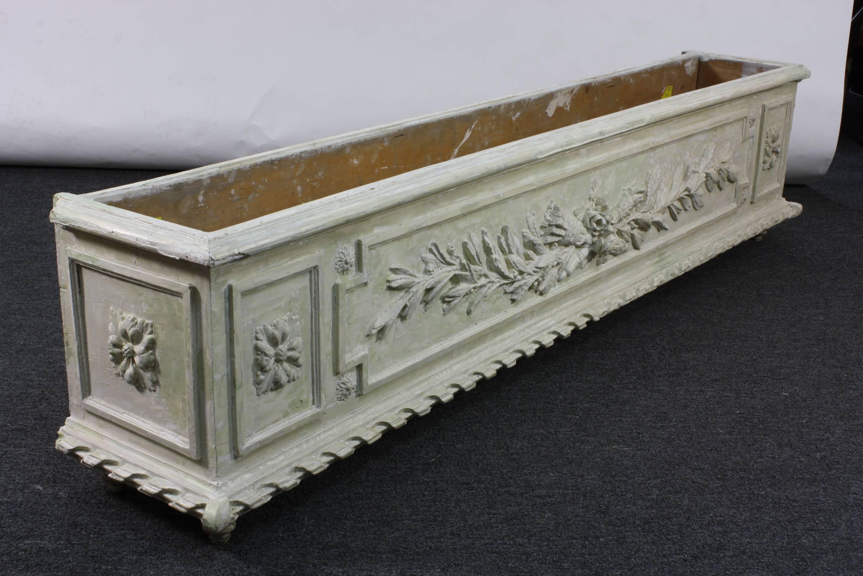 An unusually large, and deeply sculpted and painted wood planter or jardinière, in the Louis XVI style (late 19th century). The planter appears to have been stripped of some coats of paint, down to its originally grey-green paint and white gesso.