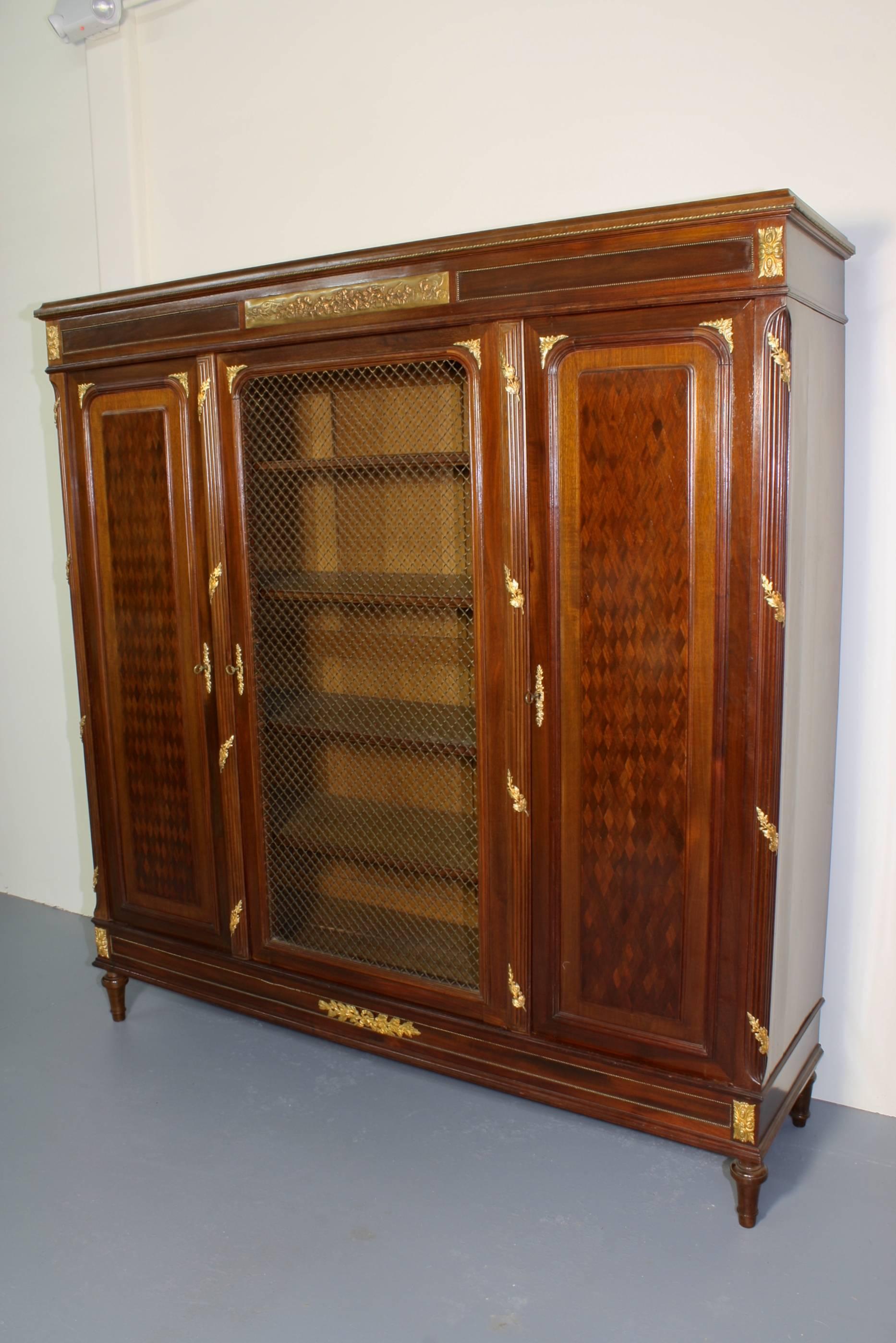 French mahogany bibliothèque or bookcase in the Louis XVI style, with two side doors, and a central door with four adjustable shelves (early 20th century) from the Faubourg Saint Antoine in Paris. The two side doors have diamond parquetry detailing,