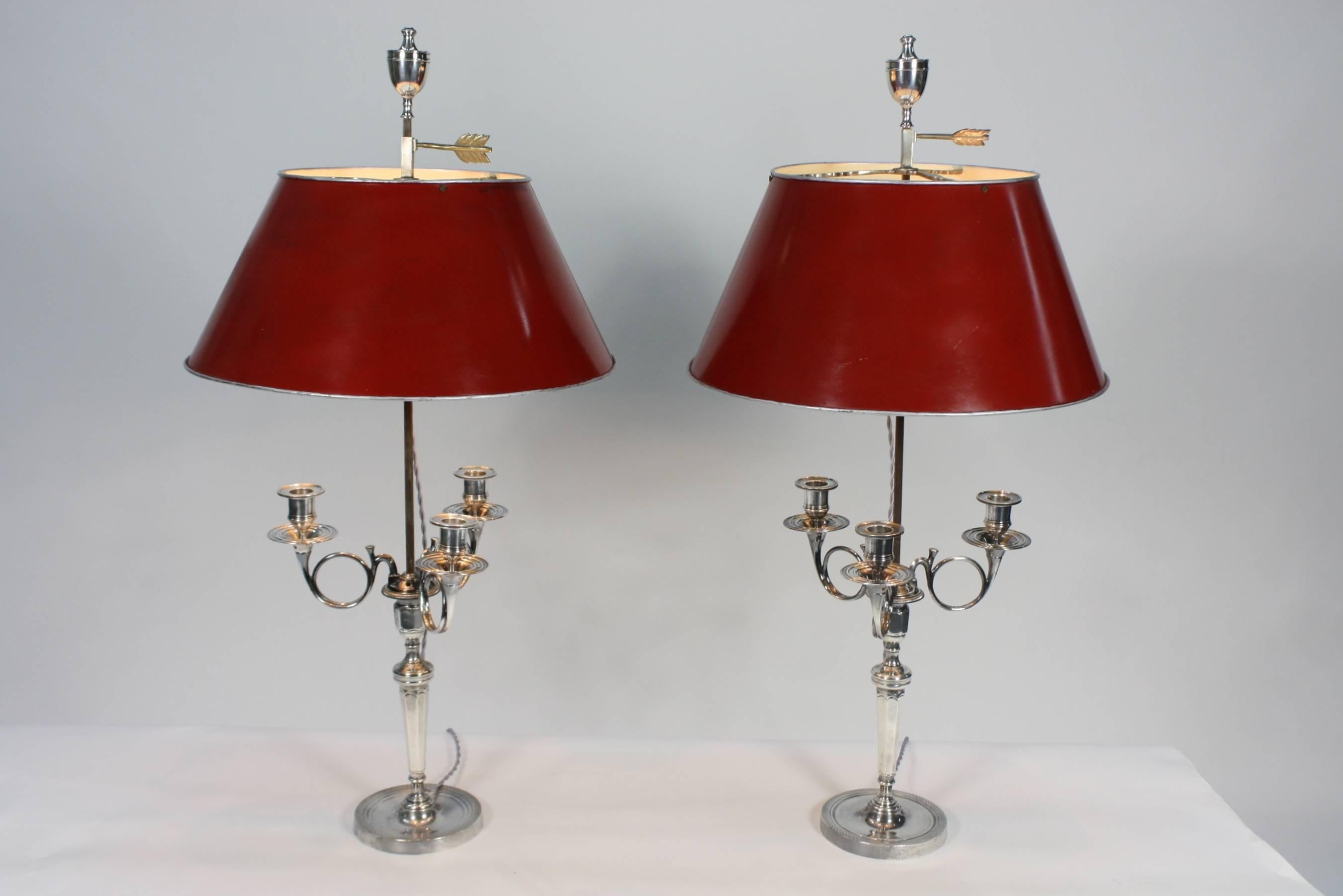 A lovely pair of neoclassical French candelabra (circa 1880), in silvered-bronze, having been converted to bouillotte lamps, with red tole shades. Each lamp has three arms for candlesticks, and the tole shade height is adjustable, decorated on top